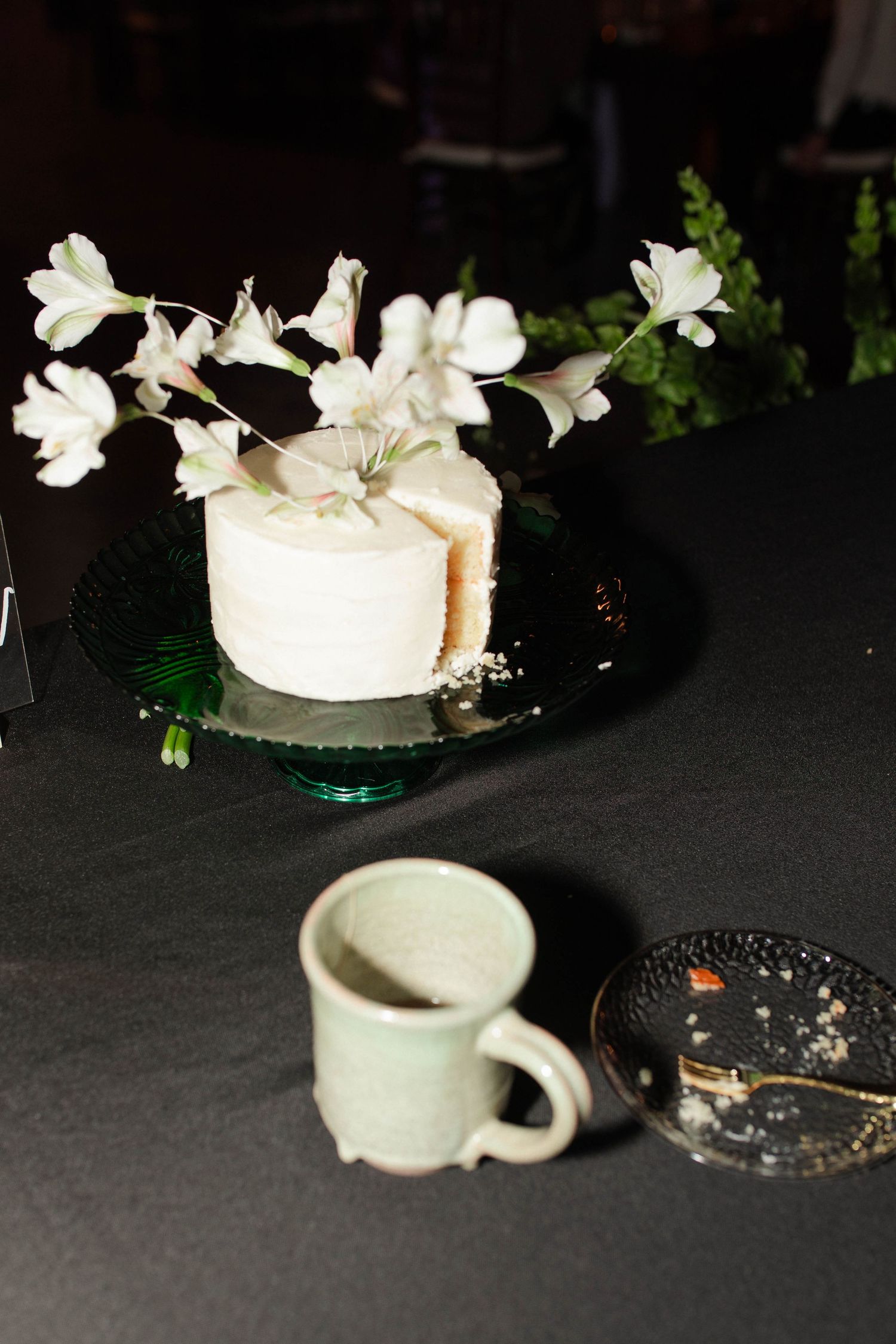 Elegant small white wedding cake with floral decorations on green glass stand beside ceramic mug micro wedding in Nashville.