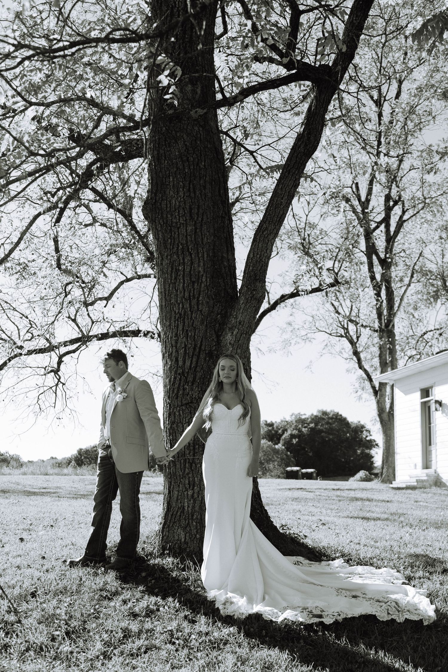 Black and white photo of bride and groom holding hands beside a large tree on their intimate Nashville wedding day.