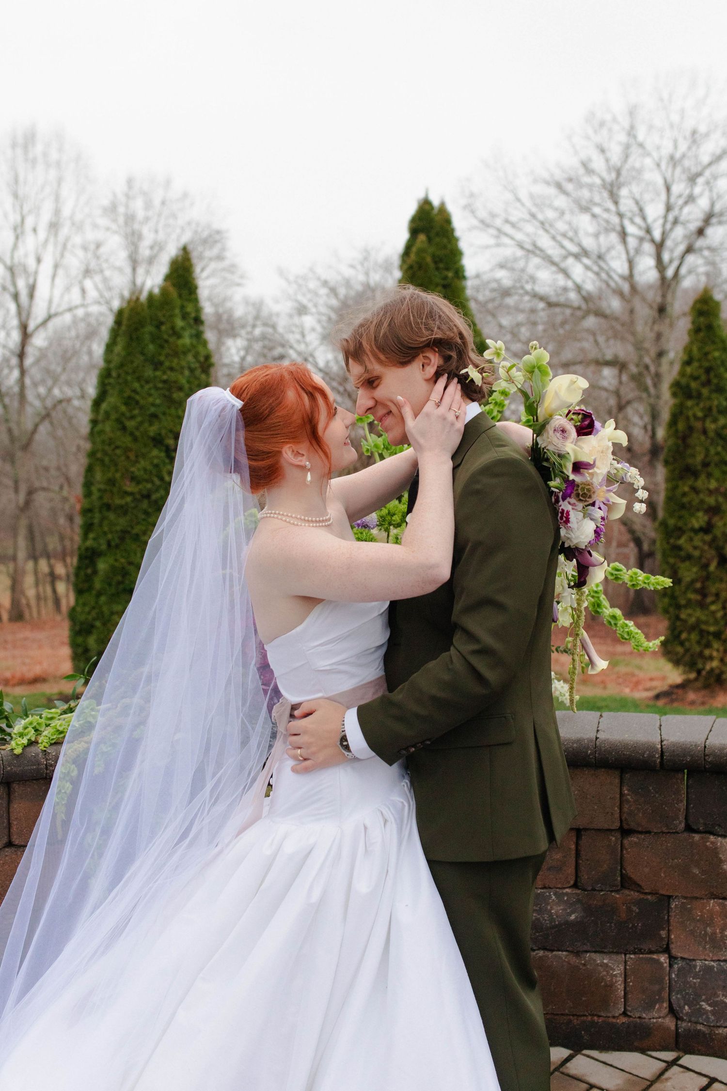 A red-haired bride and groom in a green suit embrace tenderly in an outdoor garden setting after eloping in Nashville.