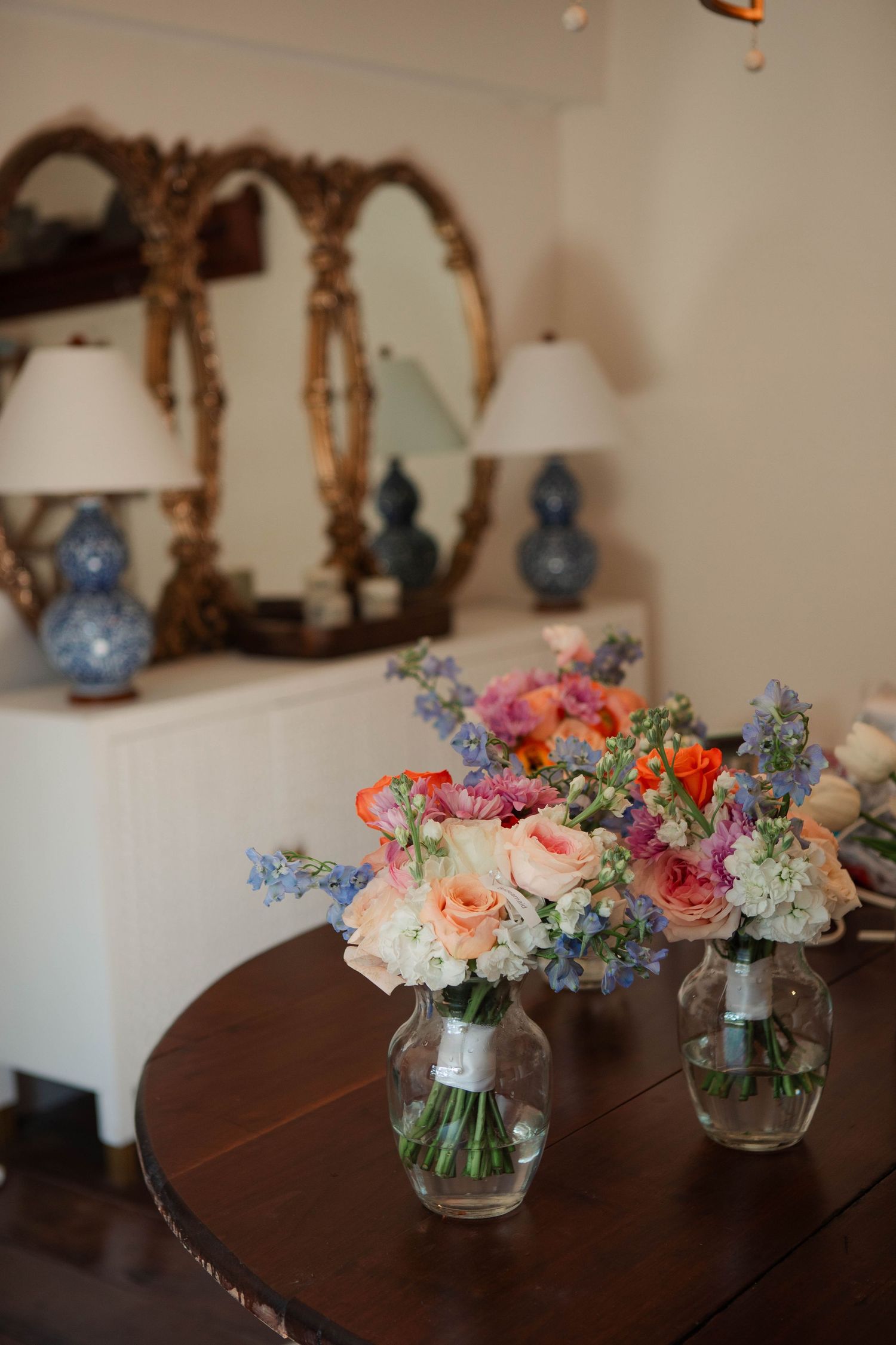 Two colorful wedding bouquets with roses and blue flowers in glass vases on a wooden table with a gold mirror backdrop.