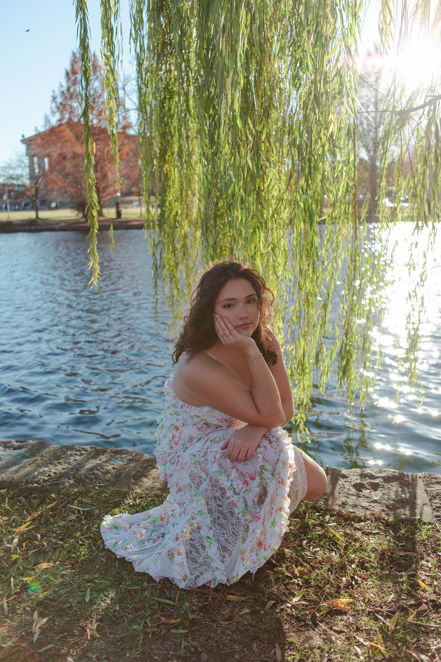 Senior graduate in floral dress sitting by a lake under a weeping willow tree in Centennial Park, Nashville.