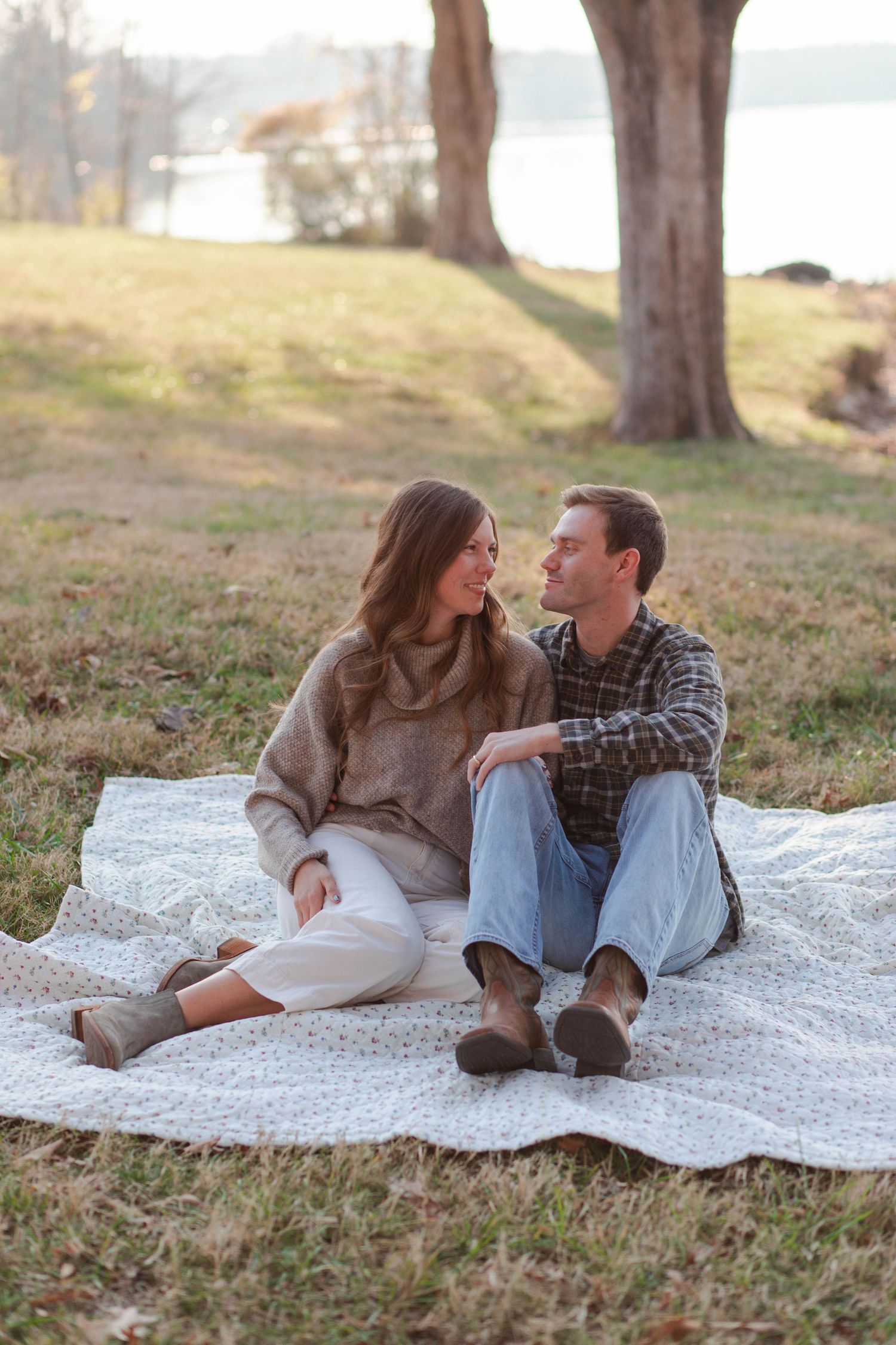 Couple relaxing on a white blanket under trees by a lake during golden hour in Nashville.