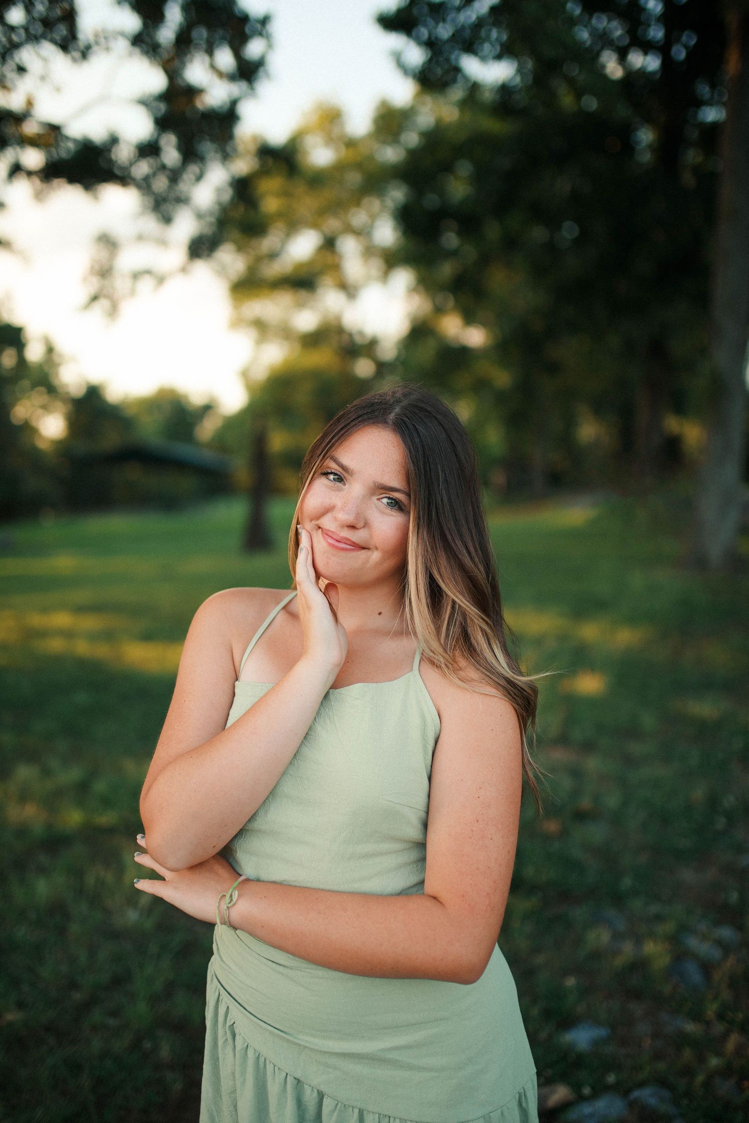 Young woman in mint green dress posing outdoors in a lush green park during golden hour.