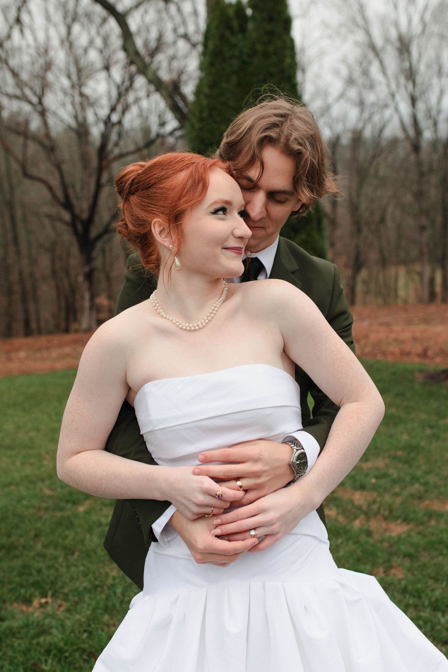 Bride in strapless white gown embraced by groom in olive suit outdoors after eloping in Nashville.