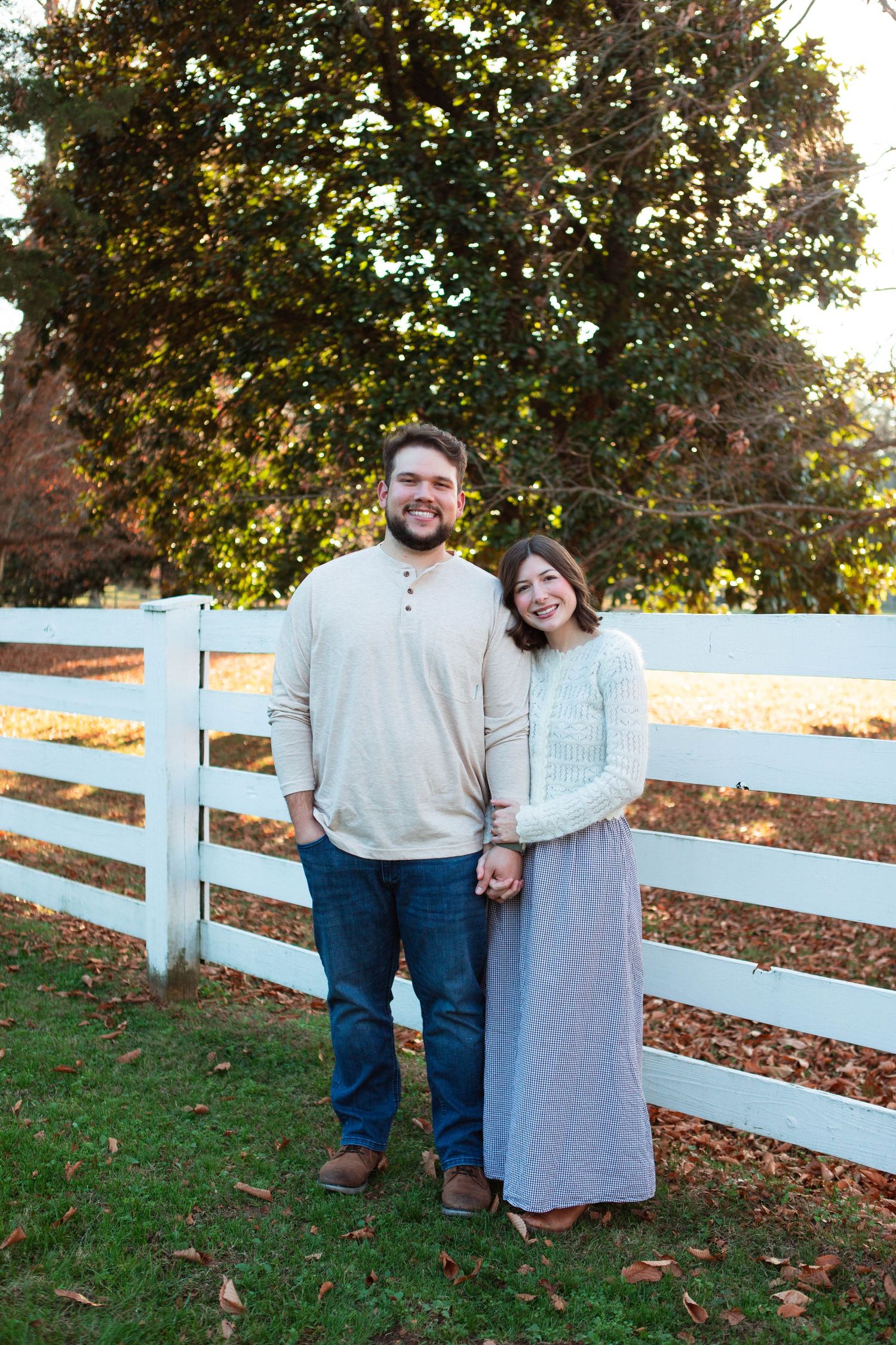 Couple poses together by a white wooden fence during an autumn outdoor photoshoot in Nashville.