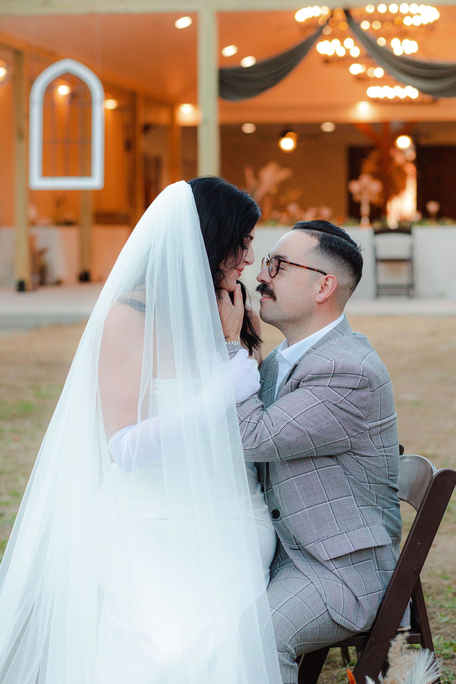 Groom in plaid suit tenderly holding brides face under veil at evening micro wedding reception in Nashville.