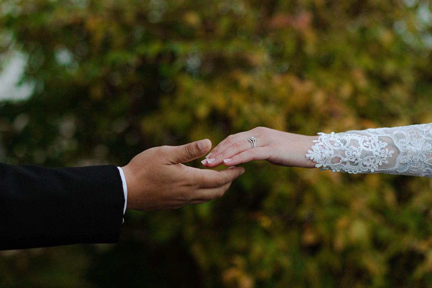 Close-up of interracial couple holding hands, bride wearing lace sleeve and wedding ring outdoors after micro wedding in Nashville.
