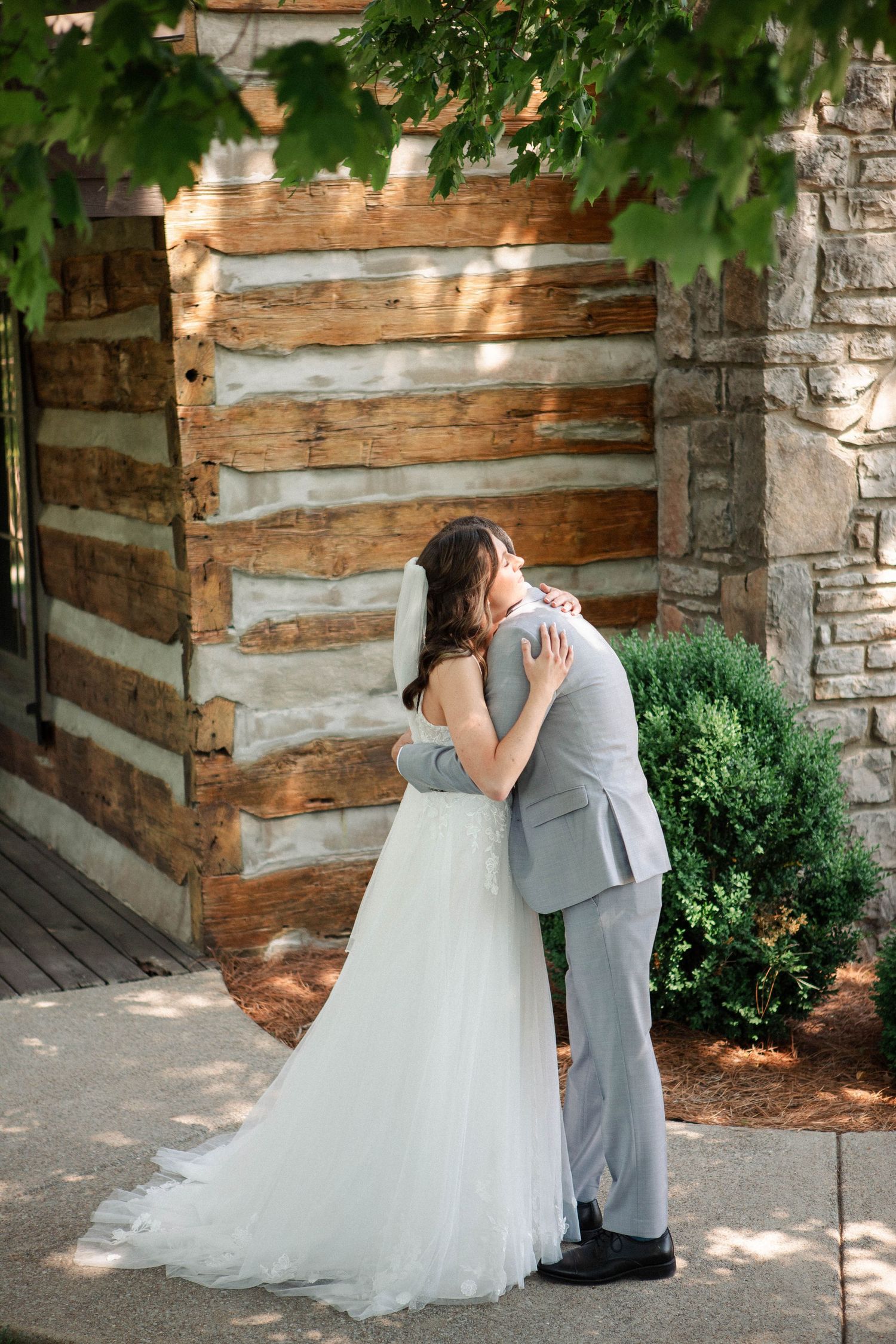 Bride and groom share a romantic embrace outside a rustic log cabin venue on their wedding day.