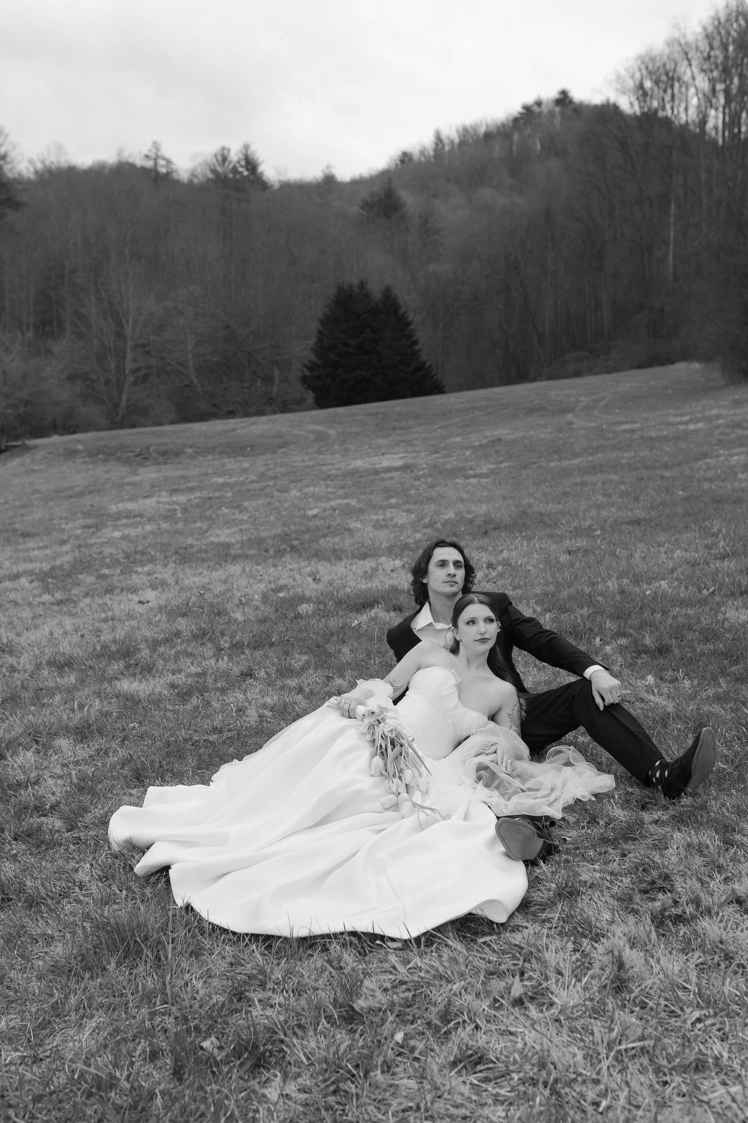 Black and white photo of bride and groom sitting together on a grassy hillside with forest backdrop  after eloping in Nashville.