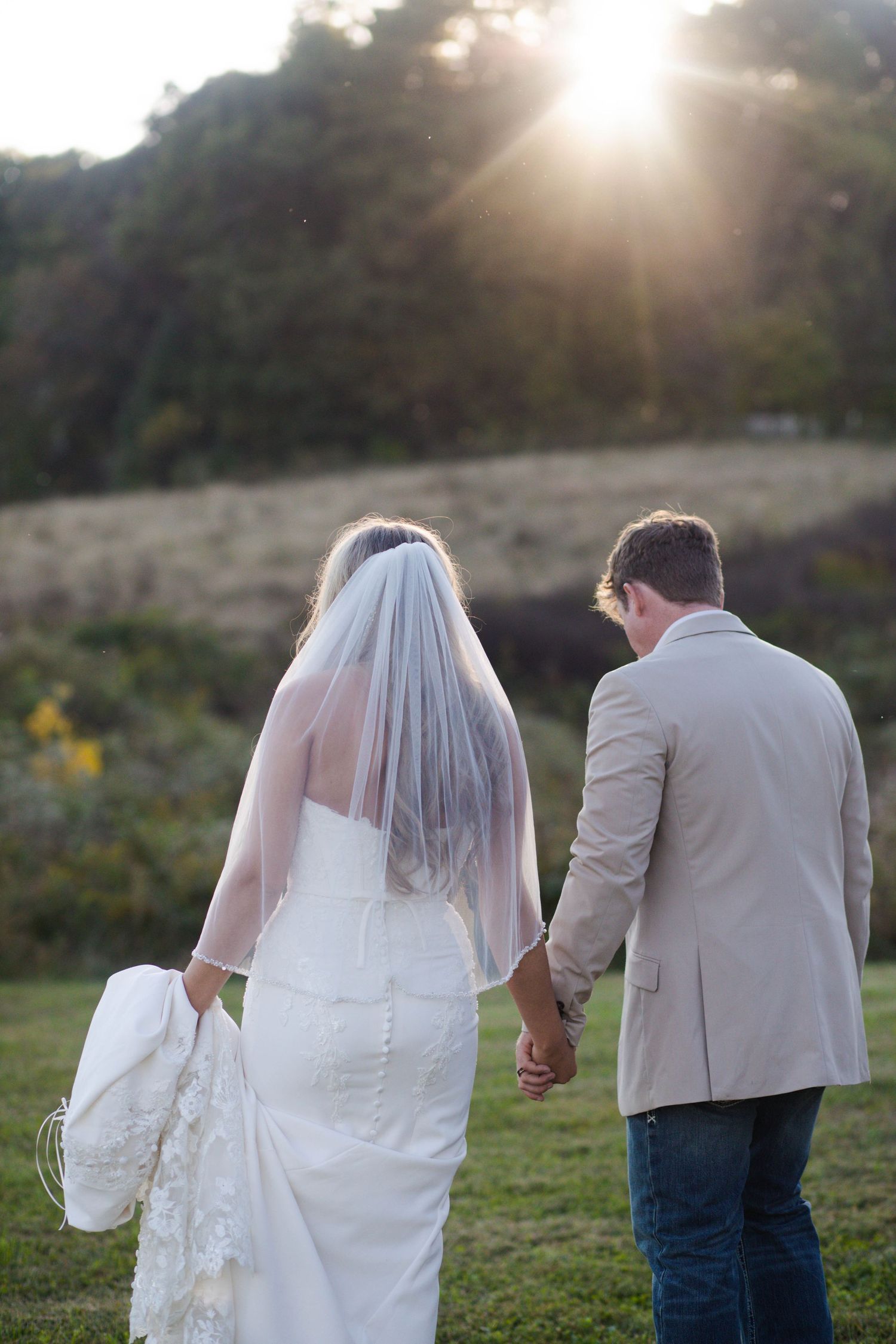 Bride and groom walk hand-in-hand toward a stunning golden sunset across an open green field after their Nashville elopement.