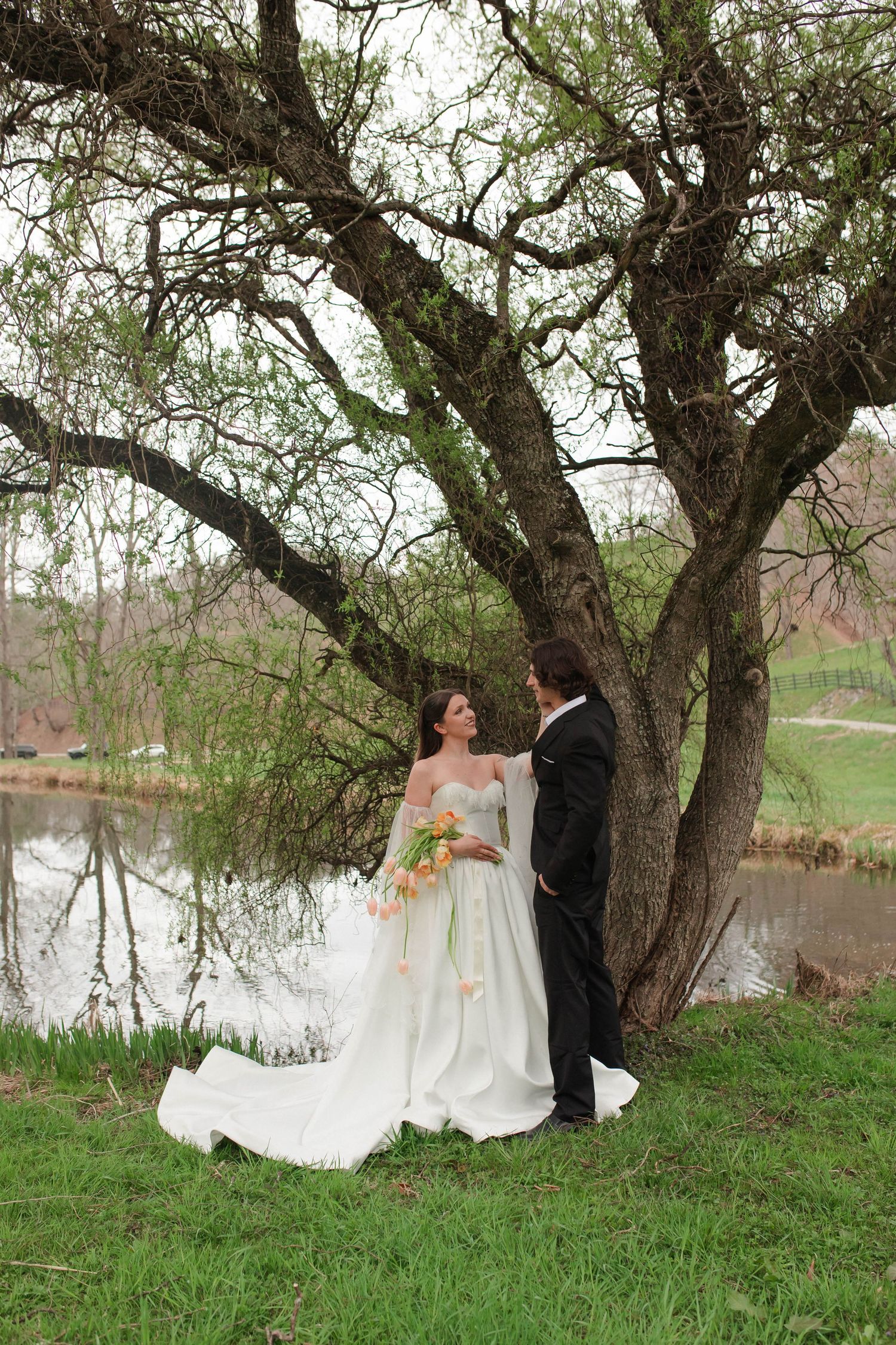 Bride and groom sharing romantic moment under willow tree near tranquil pond after eloping in Nashville.
