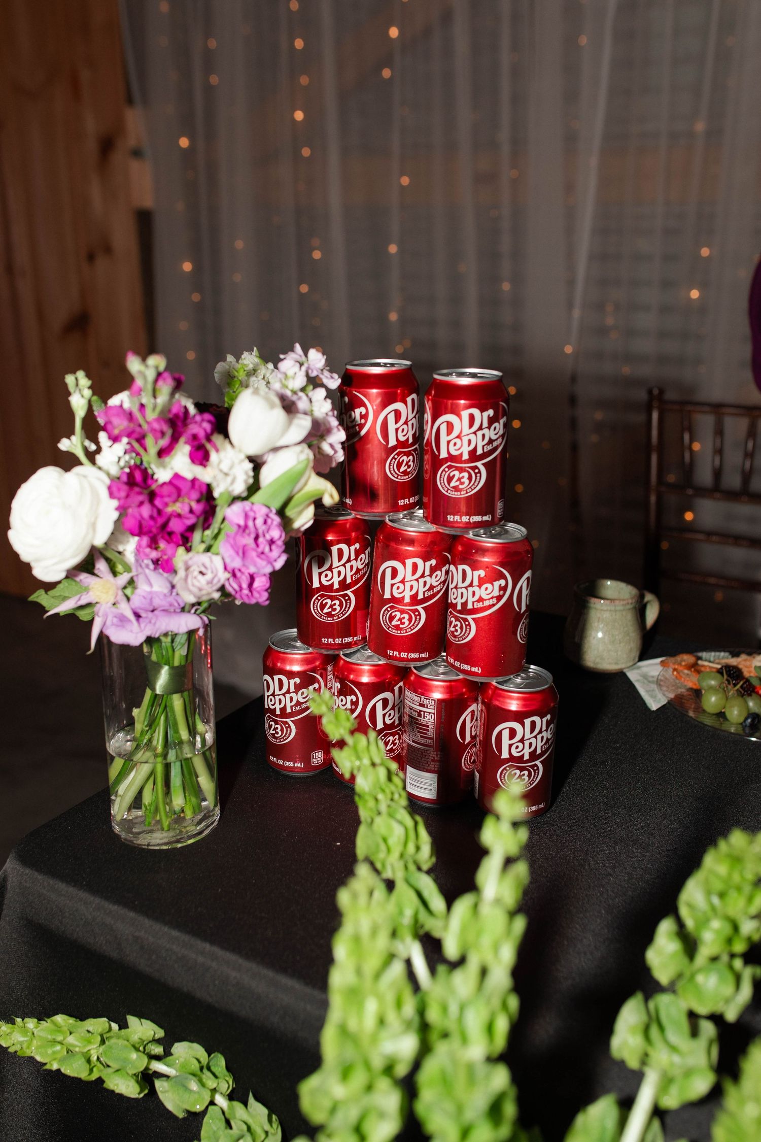 Dr Pepper cans stacked in pyramid beside purple and white floral arrangement on black tablecloth at micro wedding in Nashville.