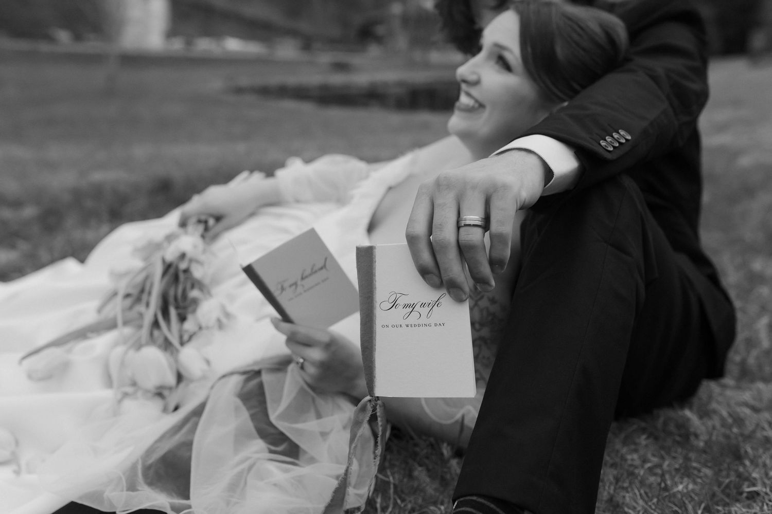 Black and white wedding photo of bride holding vow books while leaning against groom outdoors after eloping in Nashville.