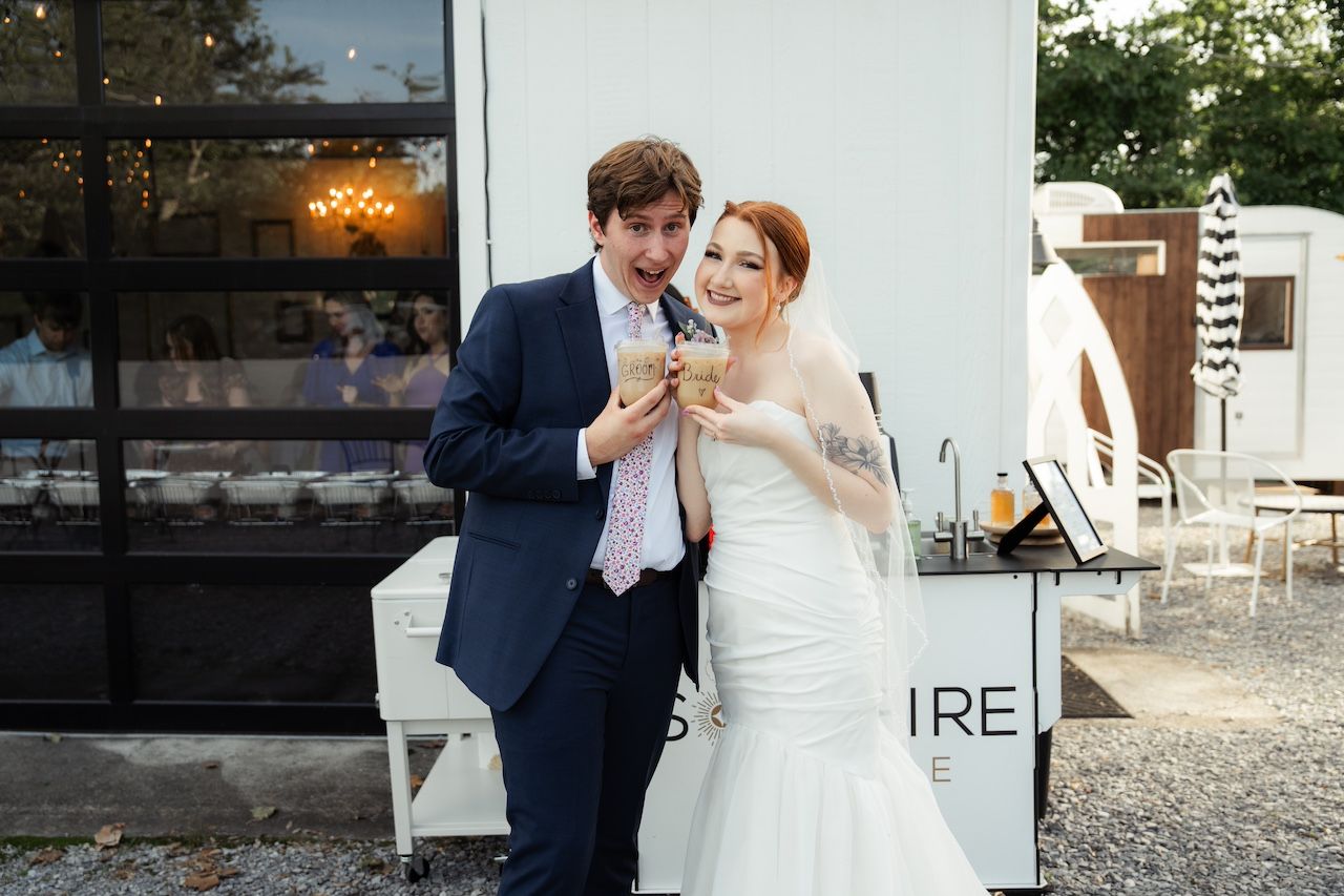 Bride and groom sharing a coffee outdoors at their intimate wedding reception, bride in white gown with veil, groom in navy suit.