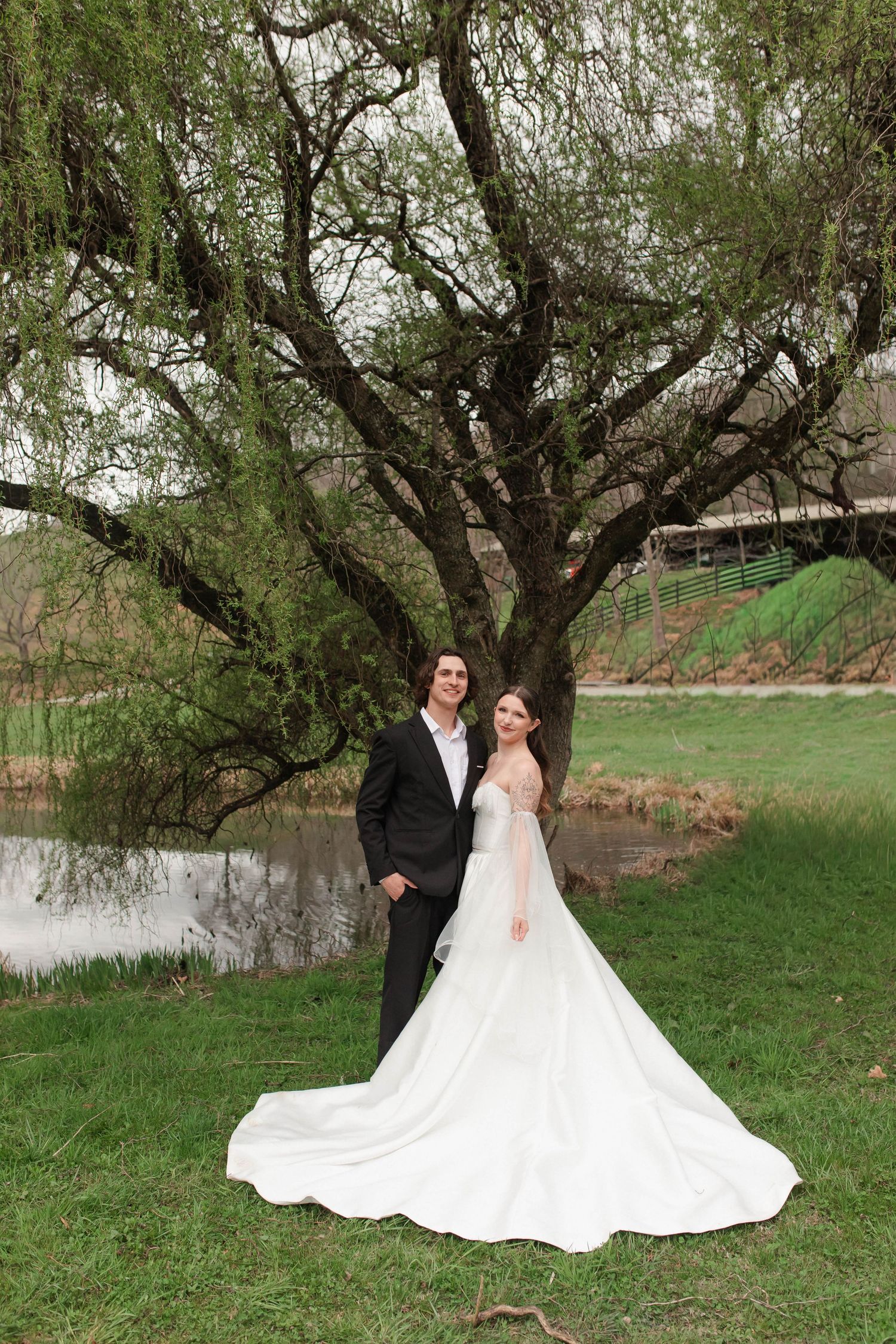 Bride and groom posing together under large willow tree beside pond after eloping in Nashville.