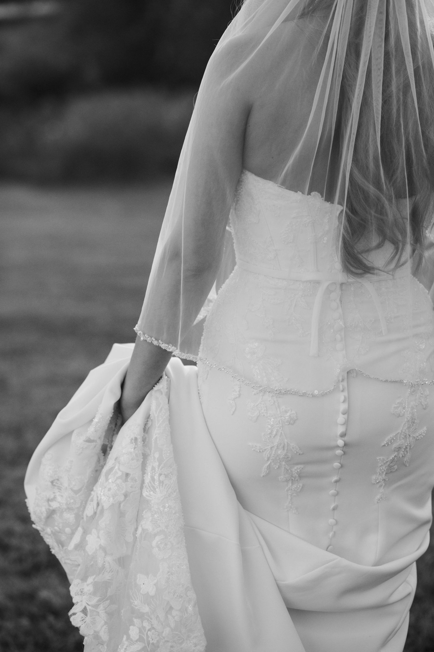 Black and white close-up of bride's lace wedding gown back detail with delicate buttons and veil.