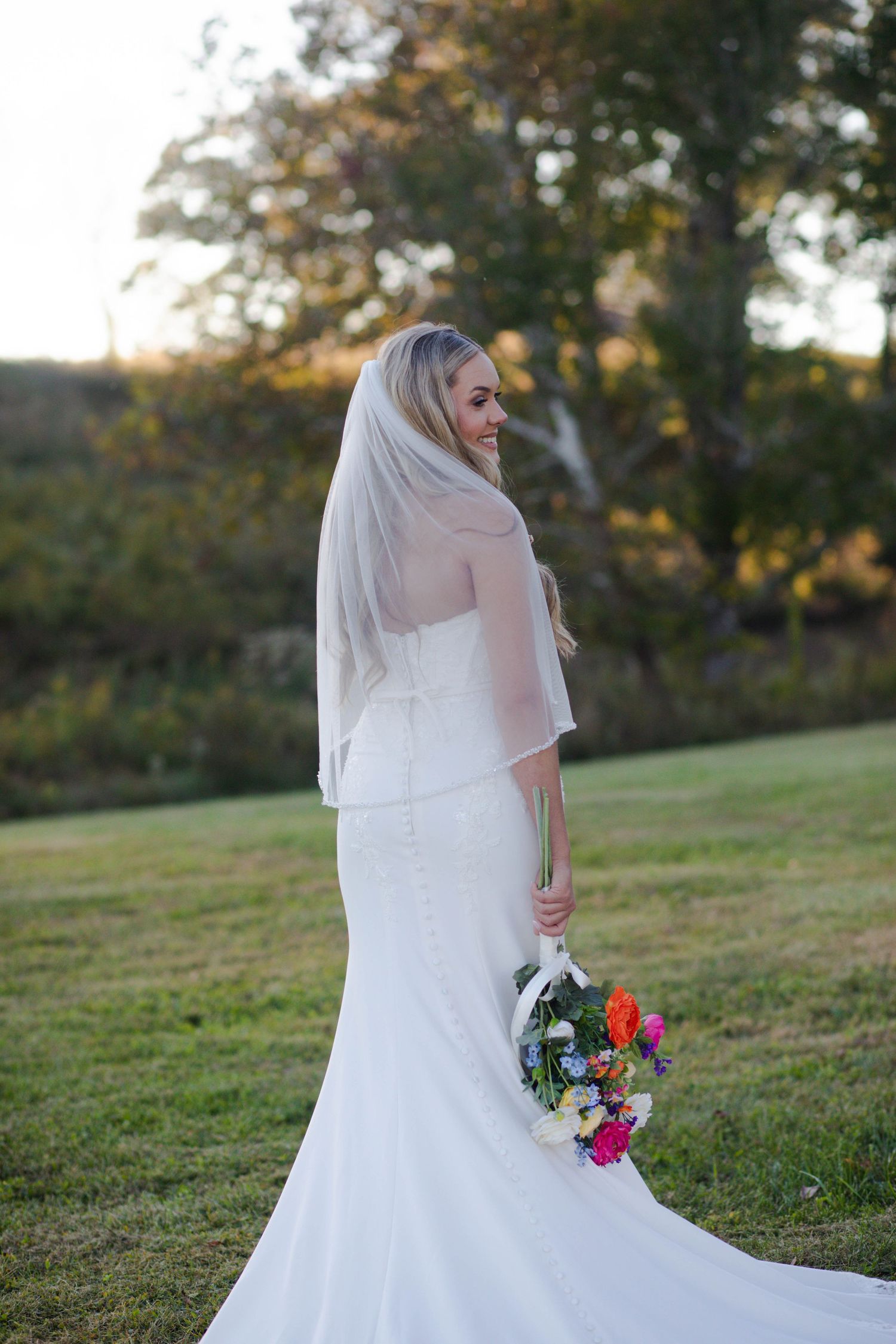 Elegant bride in fitted white gown with veil holds colorful bouquet in lush outdoor autumn setting after her Nashville elopement.