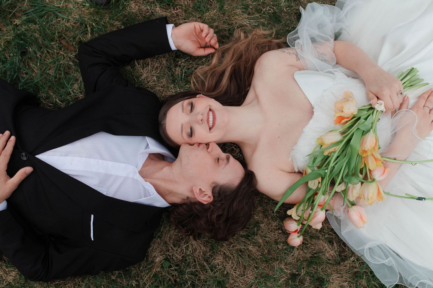 Bride and groom lying on grass, bride holding colorful tulip bouquet in white wedding dress after micro wedding in Nashville.