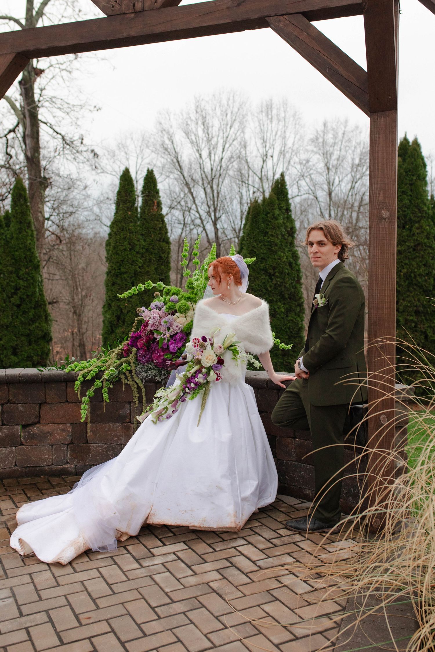 Bride and groom pose under wooden pergola with large cascading purple bouquet in winter garden setting after eloping in Nashville.