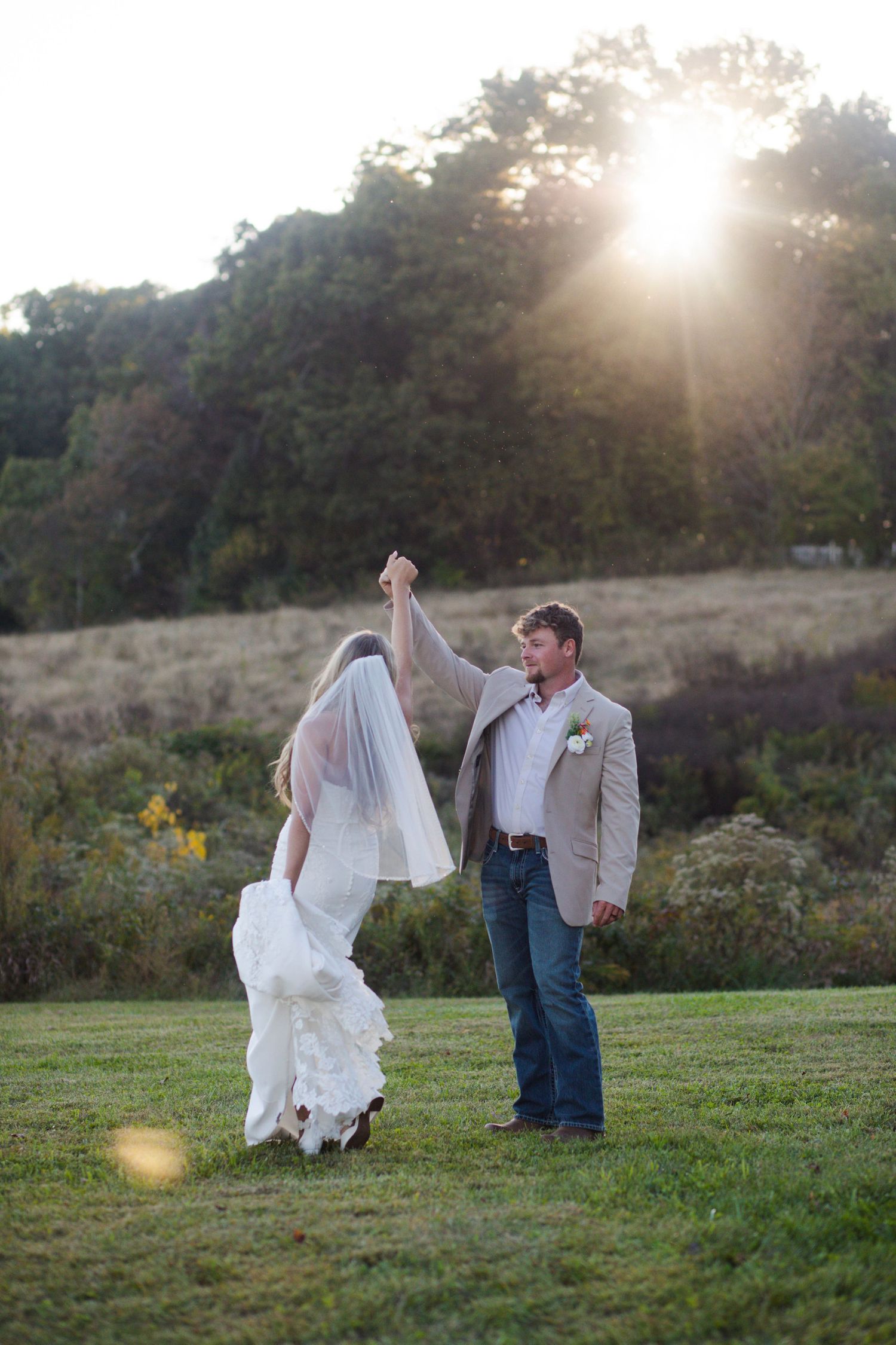 Groom twirls bride in white gown after eloping under golden sunburst in a romantic outdoor field setting in Nashville.