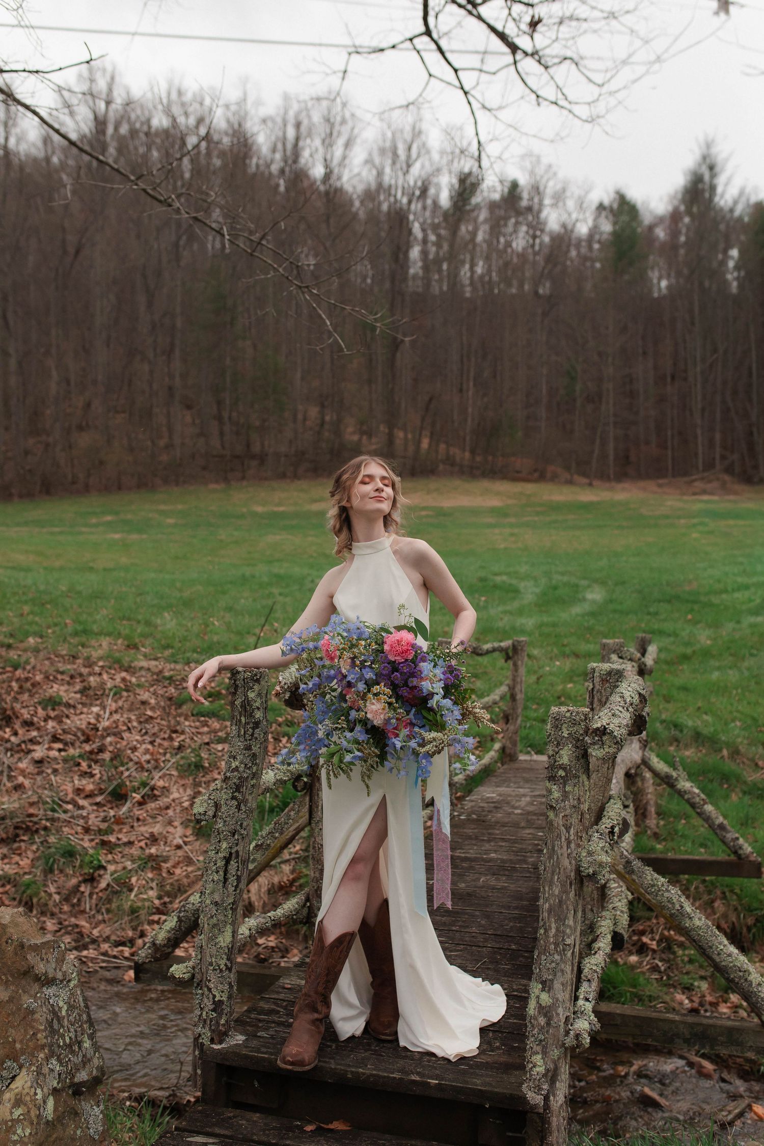 Bride in halter wedding gown holds vibrant bouquet while standing on a rustic wooden bridge outdoors after eloping in Nashville.