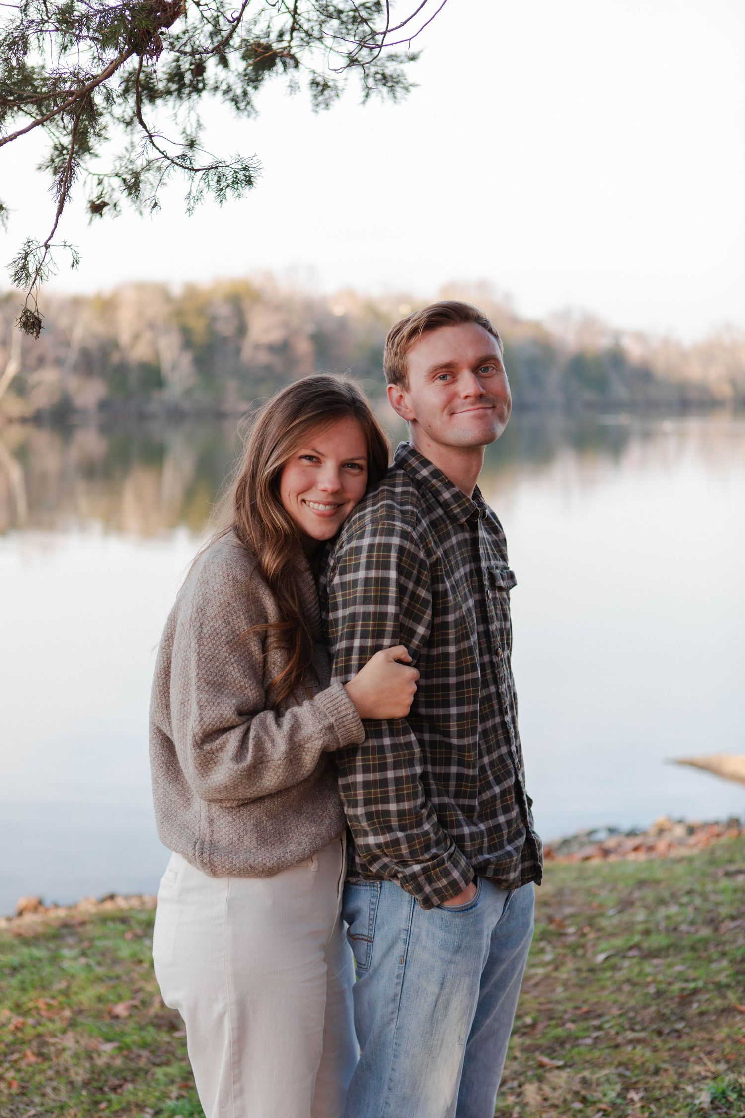 Couple embracing and smiling by a calm lake during golden hour in autumn in Nashville.