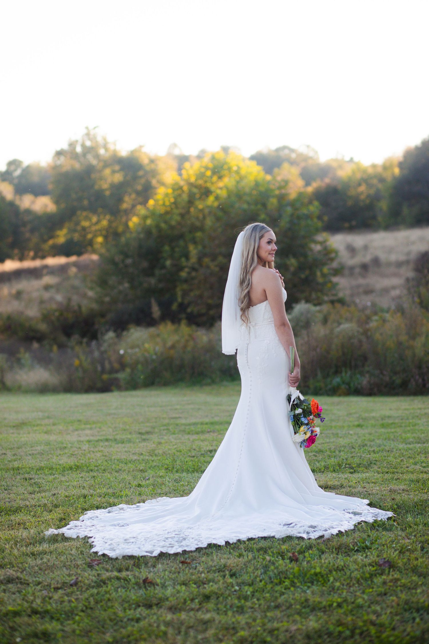 Bride in elegant white gown with lace train and veil poses gracefully in a golden sunset field after her Nashville elopement.