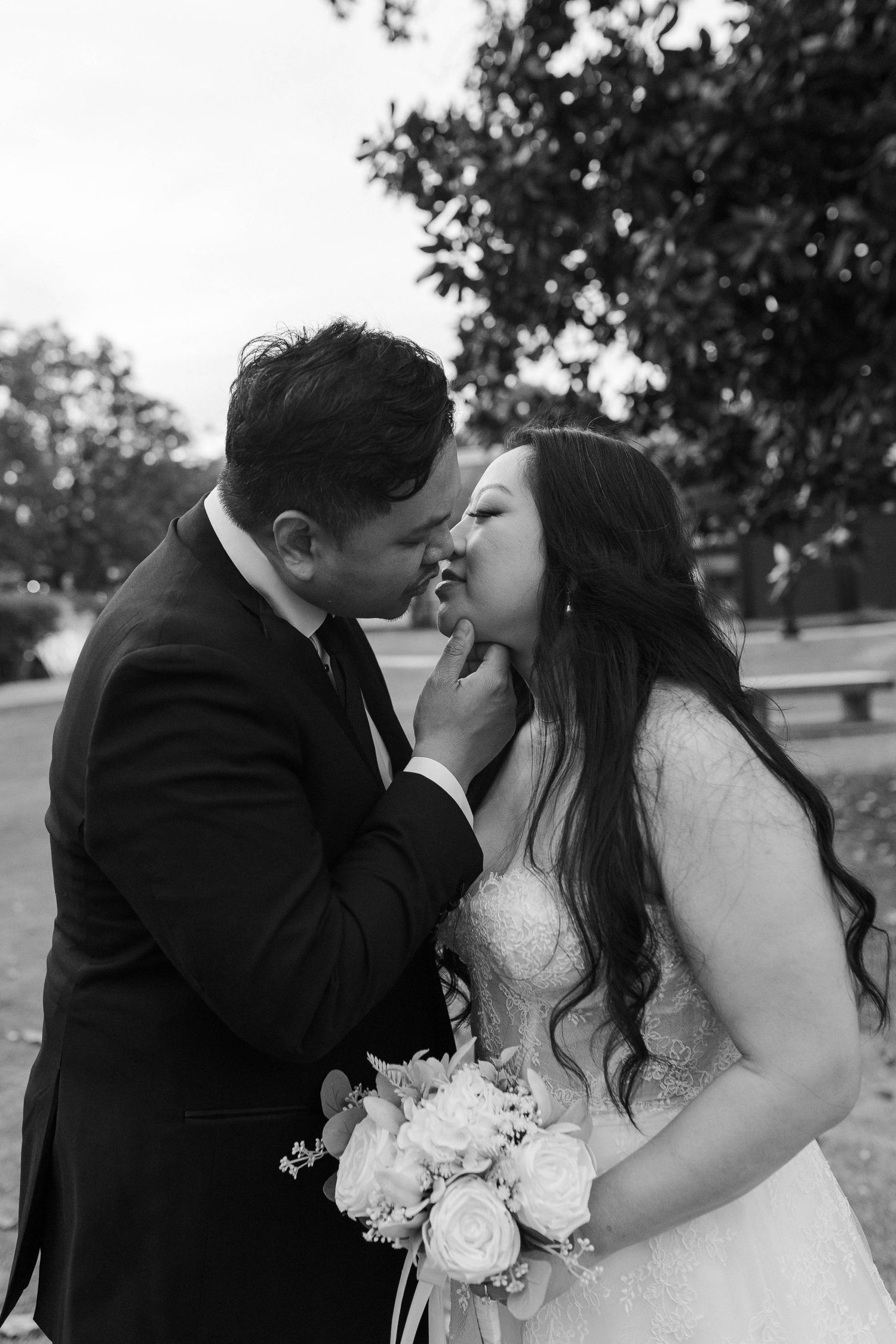Black and white photo of bride and groom sharing a kiss outdoors on their wedding day.