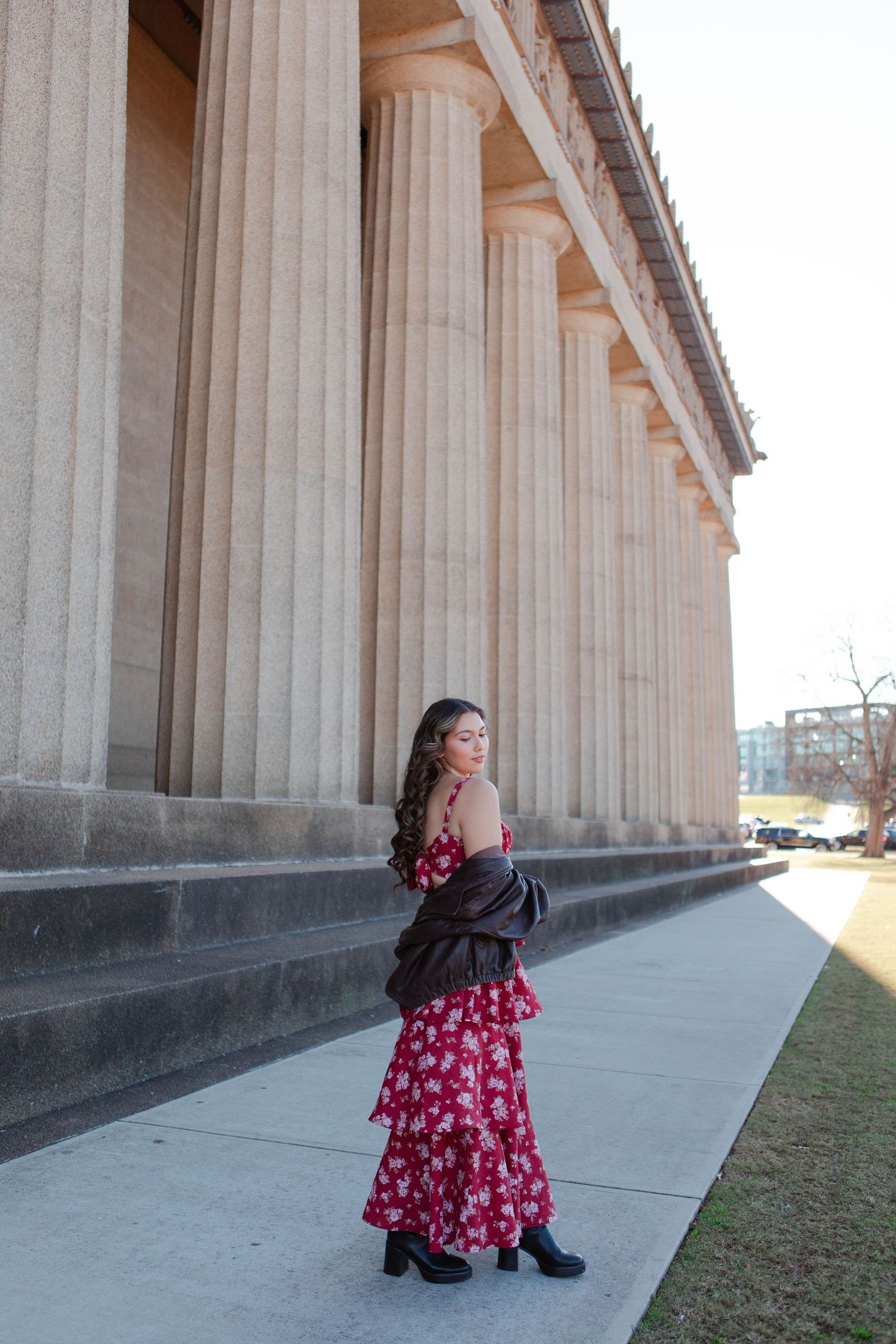 Senior graduate in red floral maxi dress posing beside large stone columns of the Parthenon in Nashville.