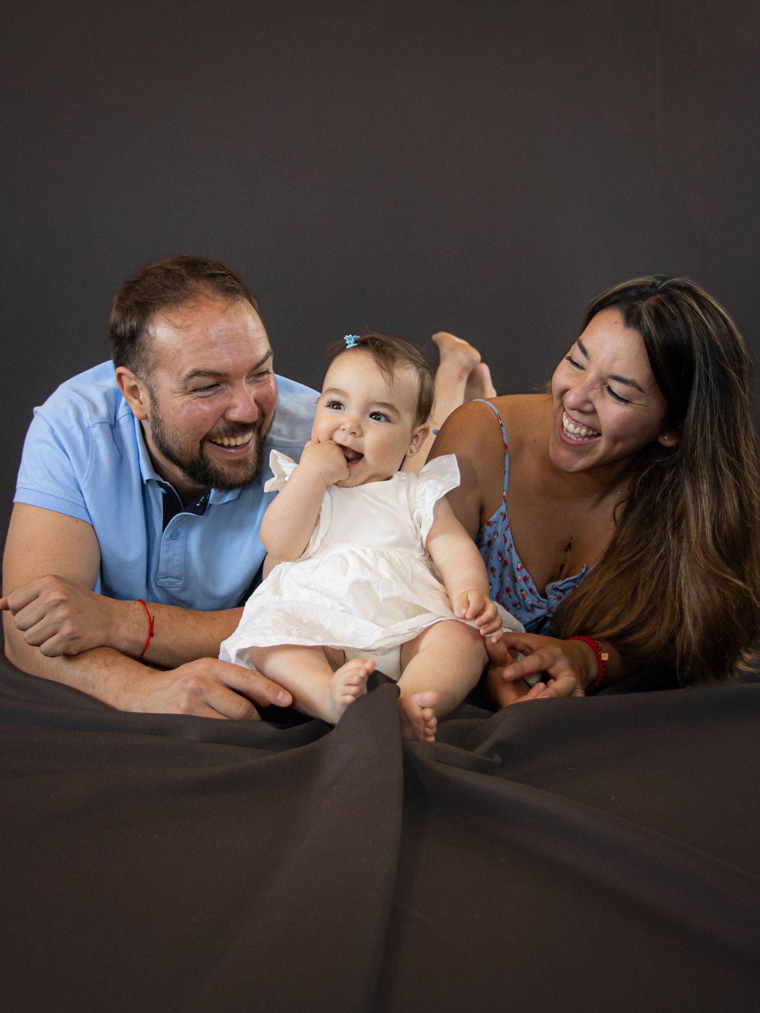 Fotografía familiar natural en estudio, sesión de fotos de padres y bebé acostados.