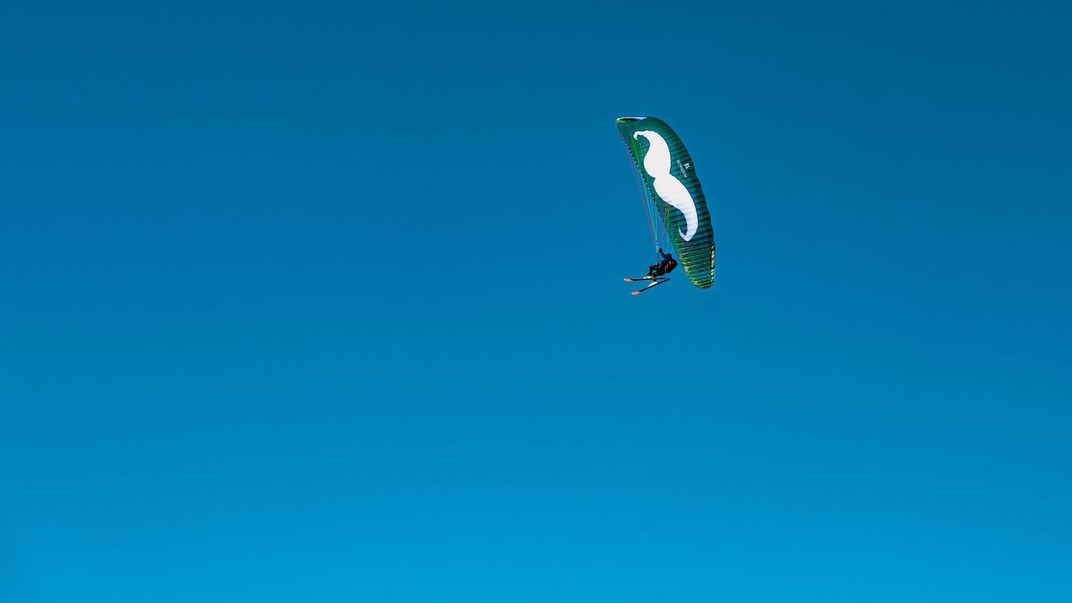 Person paragliding with a black and white canopy against a clear bright blue sky.
