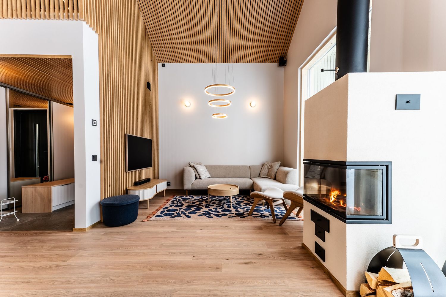 Scandinavian living room with wood-paneled ceiling, corner fireplace, sectional sofa, and large windows.