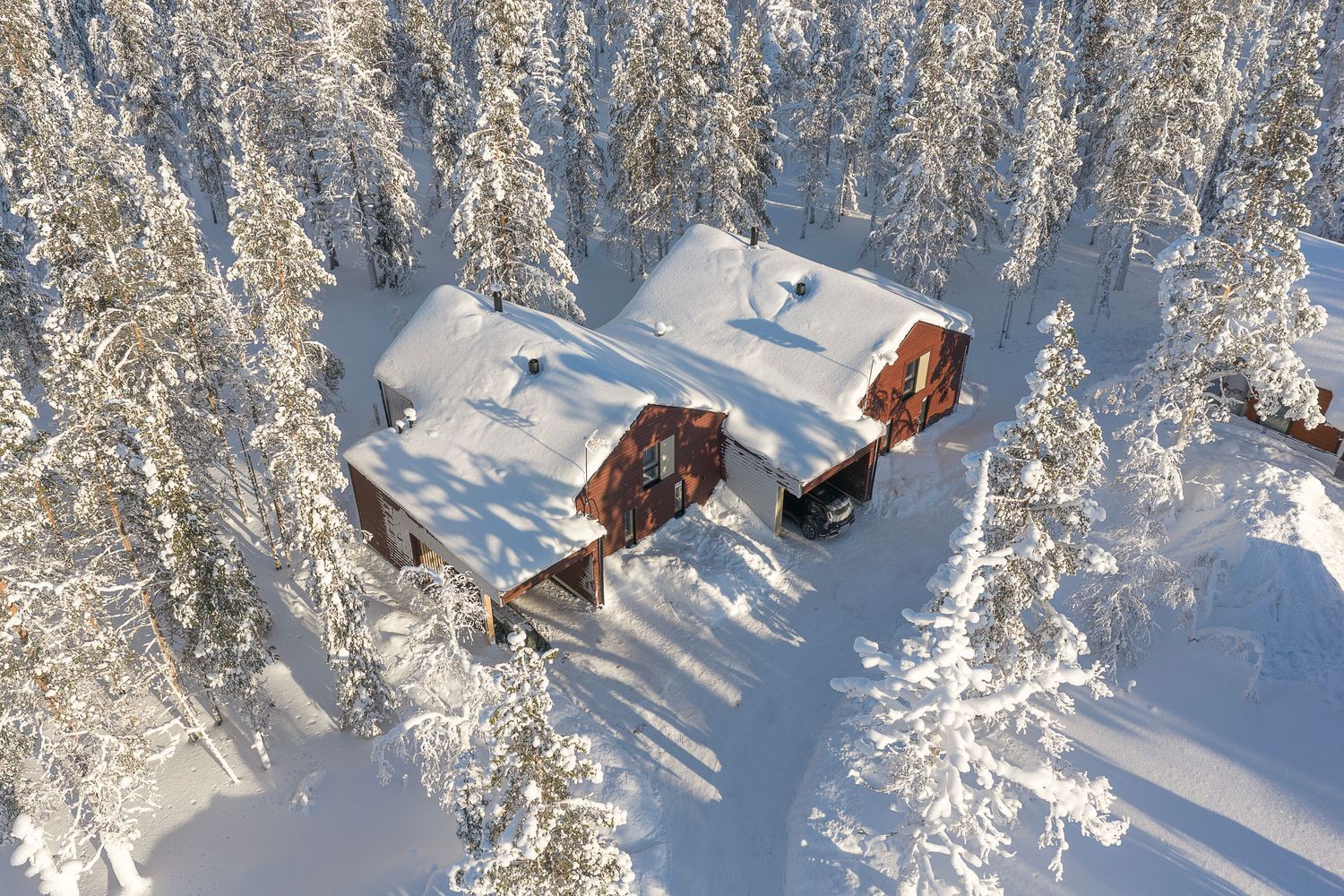 Aerial view of a snow-covered cabin surrounded by frost-laden pine trees in a winter forest landscape.