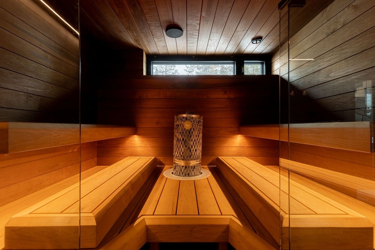 Traditional Finnish sauna interior with tiered wooden benches, cylindrical stone heater, and warm golden lighting.