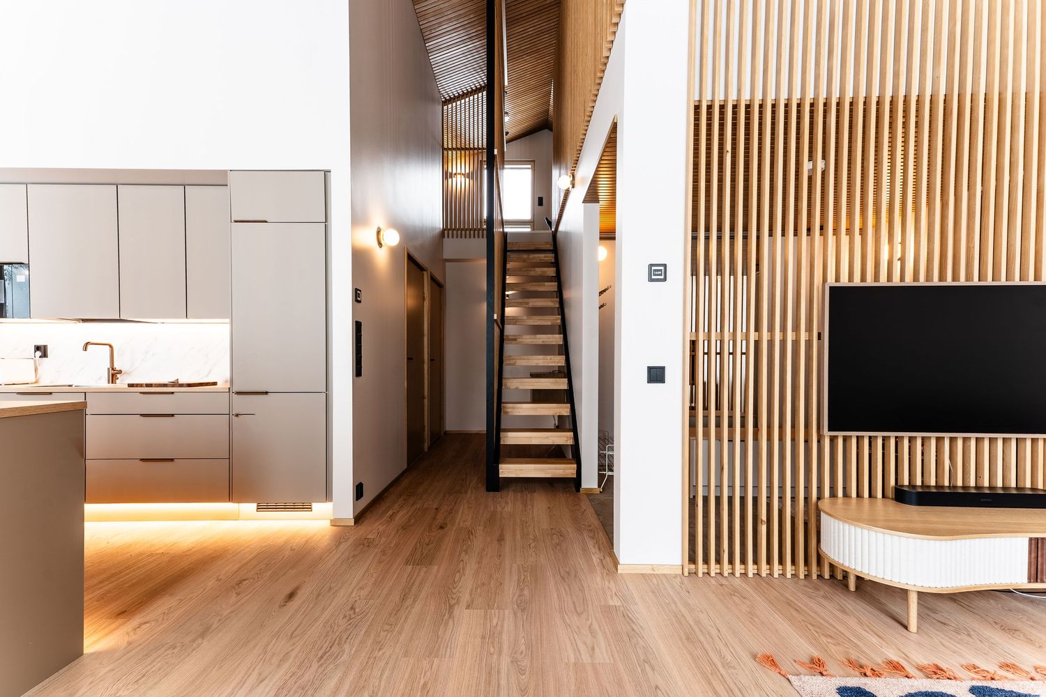 Modern Nordic interior with taupe kitchen, wood slat partition, staircase, and light oak flooring.