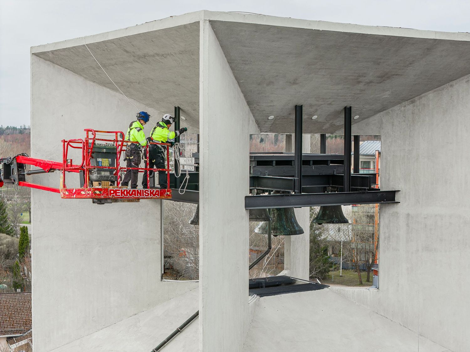 Construction workers on a red aerial lift platform inspect concrete structure at a building site.