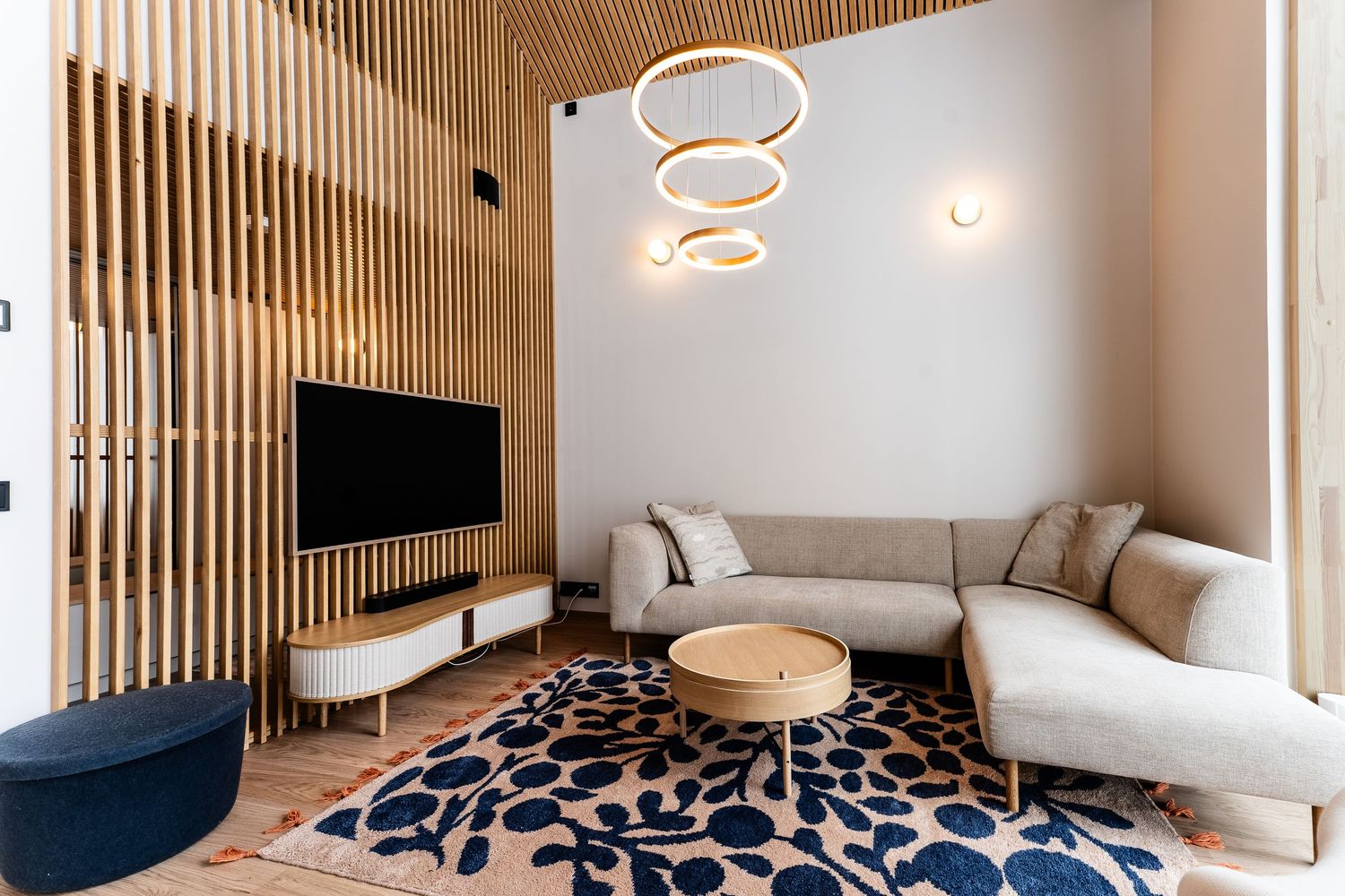 Contemporary Scandinavian living room with wood slat wall, sectional sofa, ring lights, and floral rug.