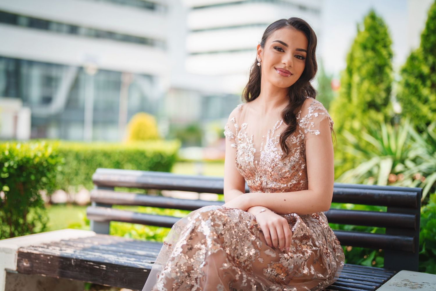 Elegant sequined rose gold dress photographed on a garden bench with modern architecture in background.