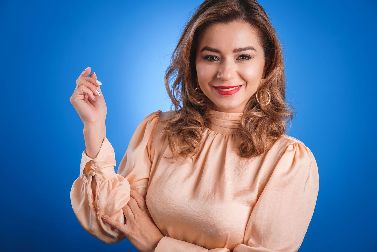Woman in peach blouse poses professionally against blue background.