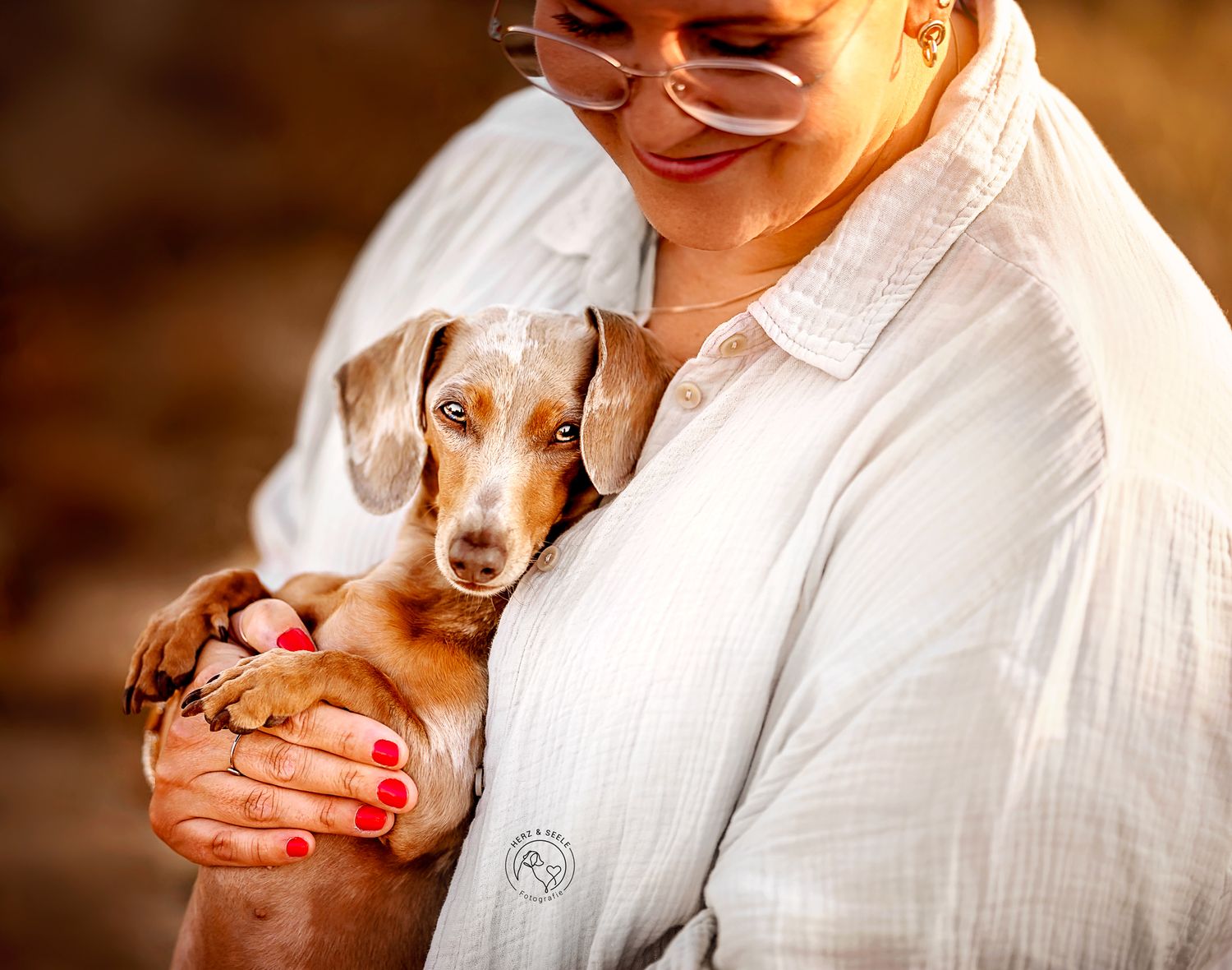 Woman cradling tiny Dachshund puppy with red manicured nails outdoors.