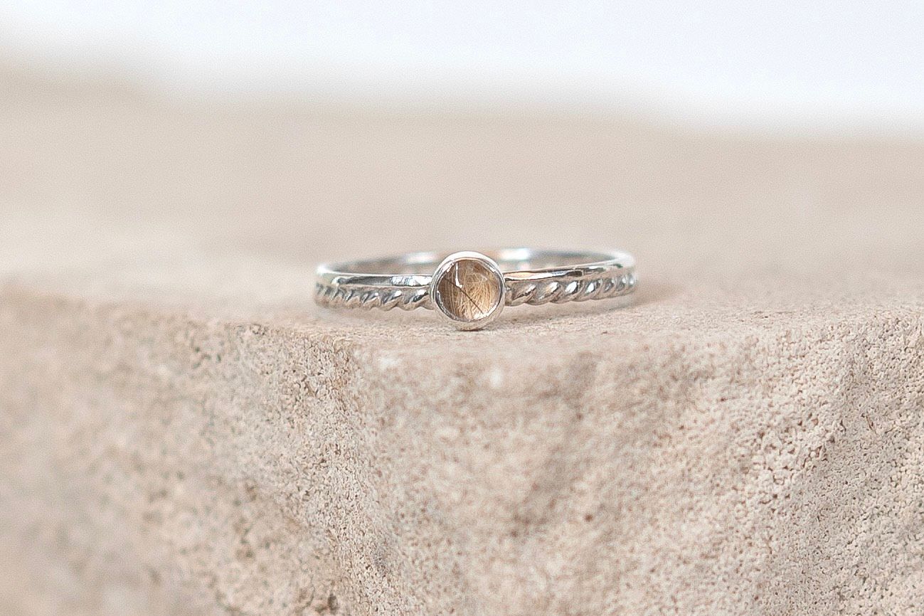 Silver stacking ring with champagne gemstone and twisted band detail resting on a stone surface.