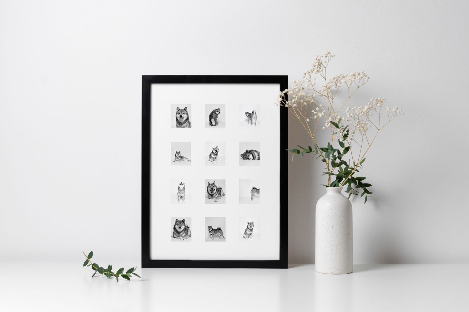Black framed grid of twelve detailed pencil drawn animal portraits leaning against white wall with decorative vase.
