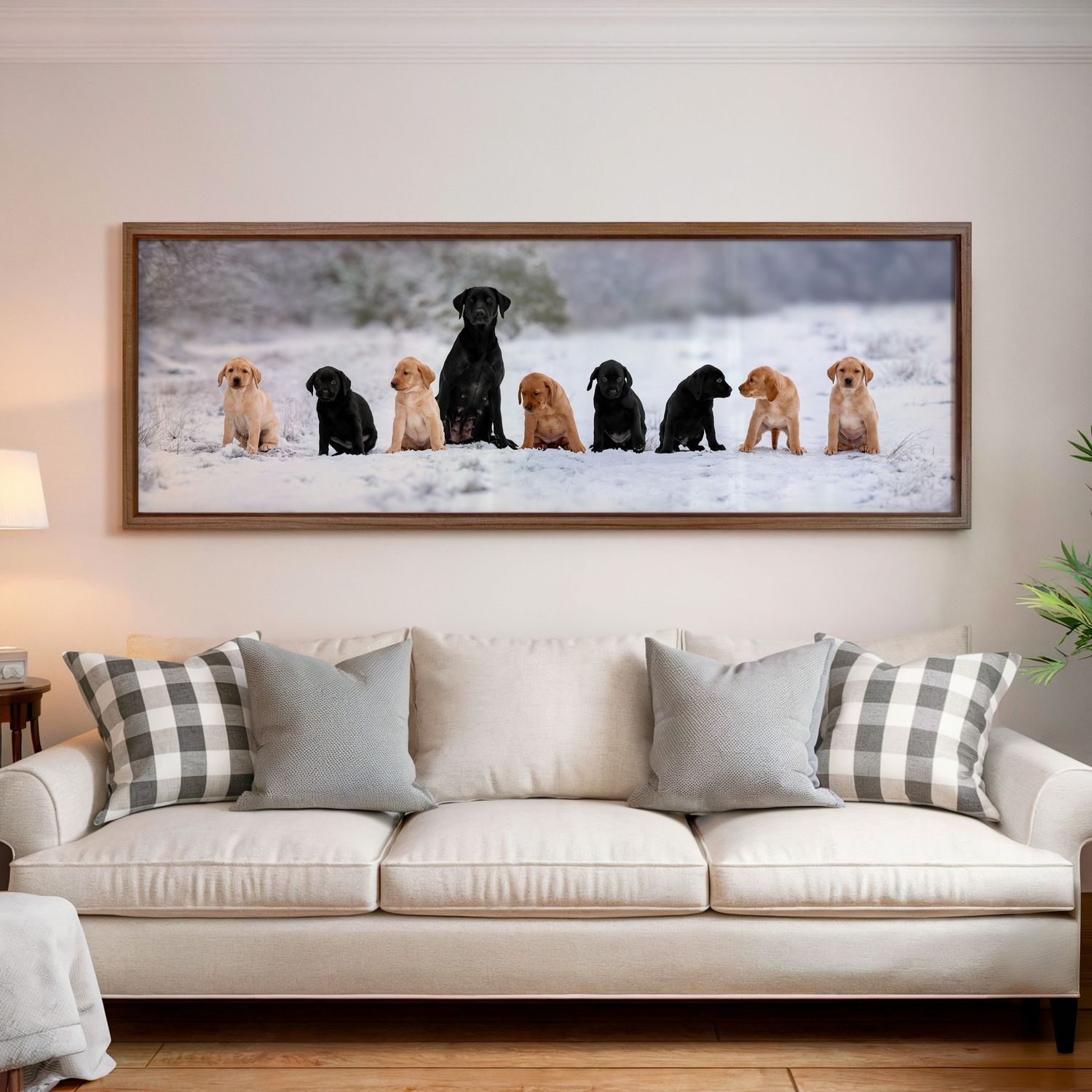 Panoramic framed print of Labrador puppies sitting in snow, displayed above a beige sofa.