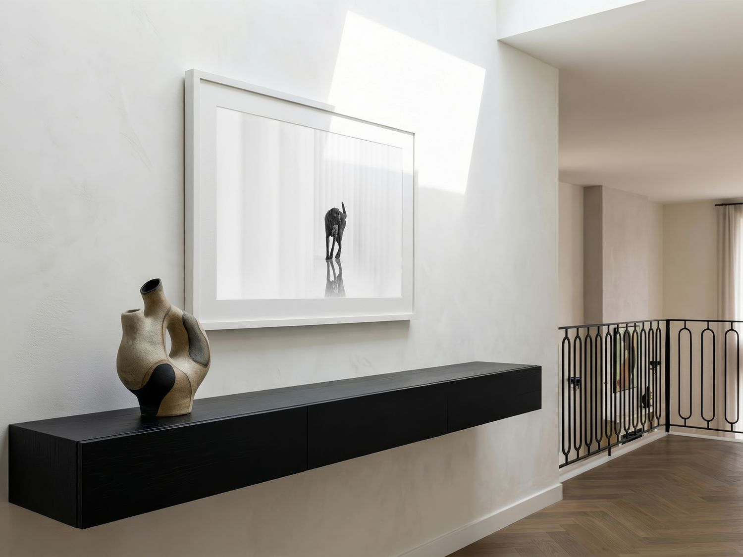 Minimalist modern hallway with black floating console, sculptural decor, and framed dog artwork on wall.