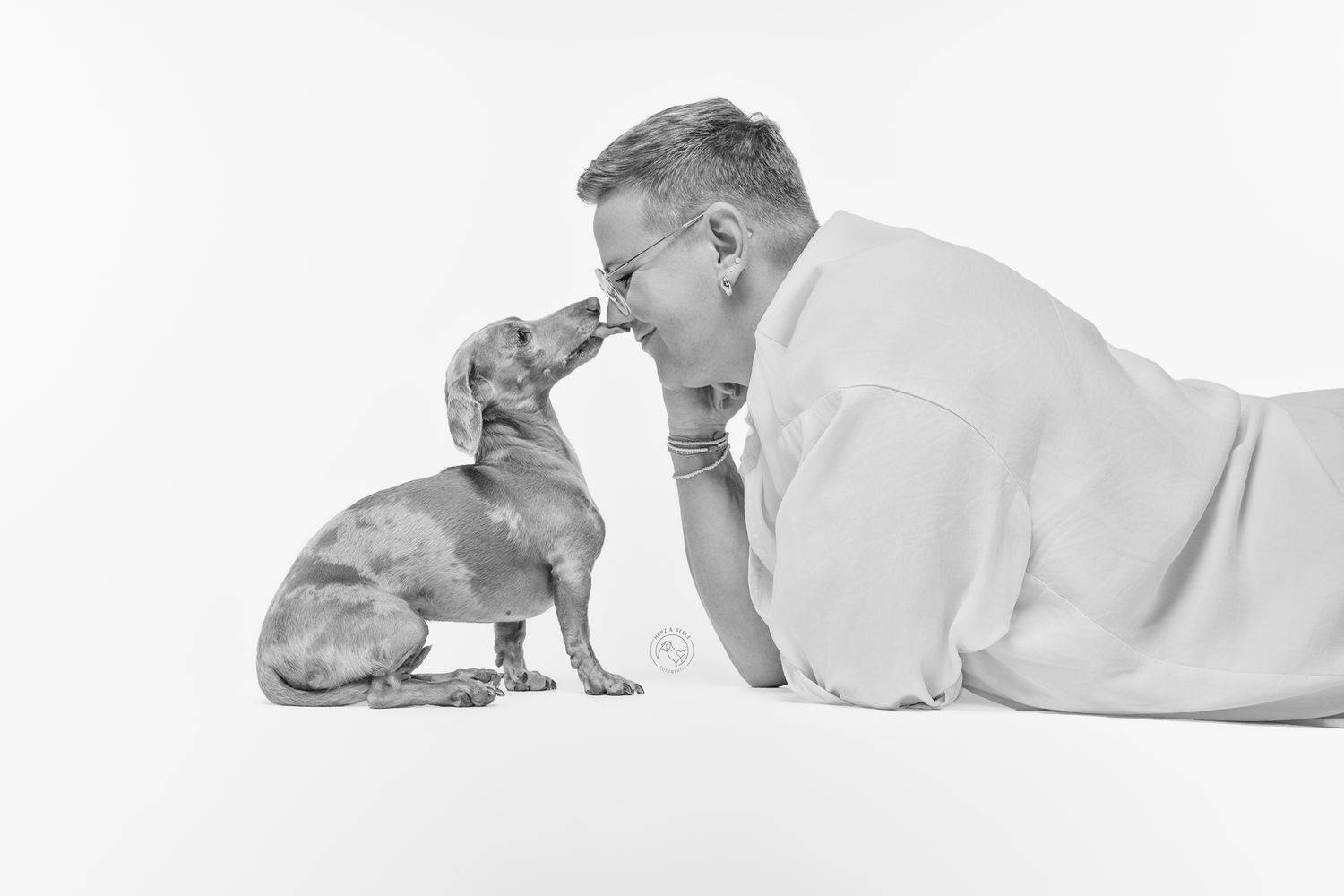 Black and white image of man and dachshund touching noses face to face.