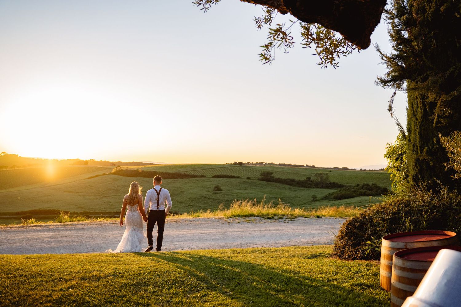 Couple holding hands at sunset overlooking rolling green hills at a romantic outdoor wedding venue.