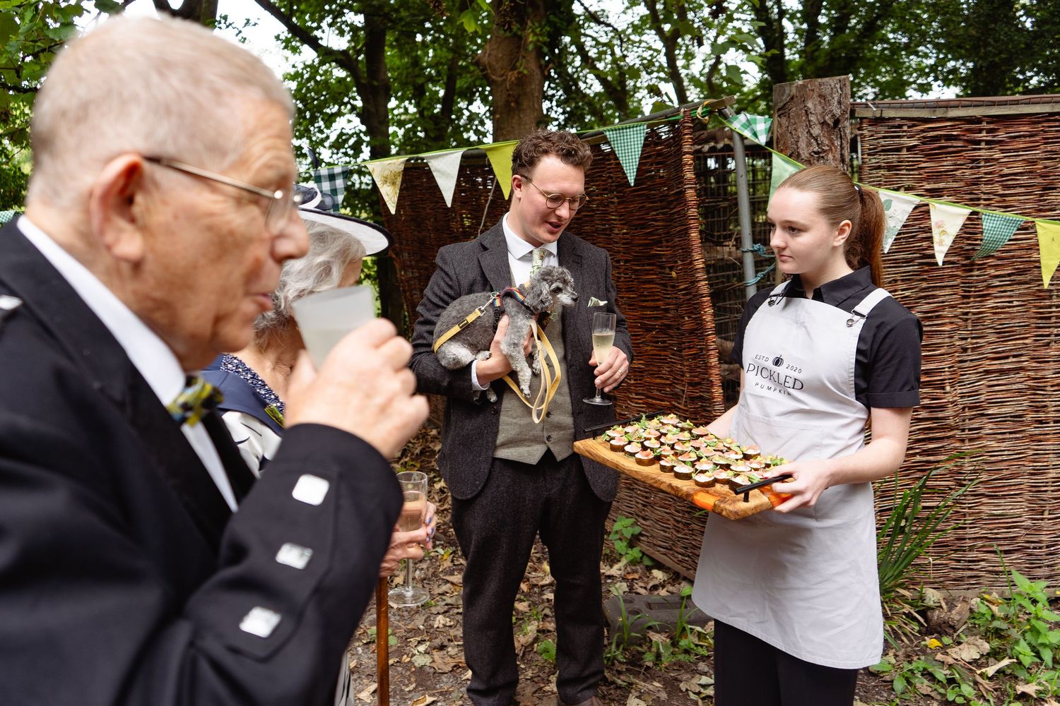 A waitress serves appetizers on a tray to guests at an outdoor garden party event.