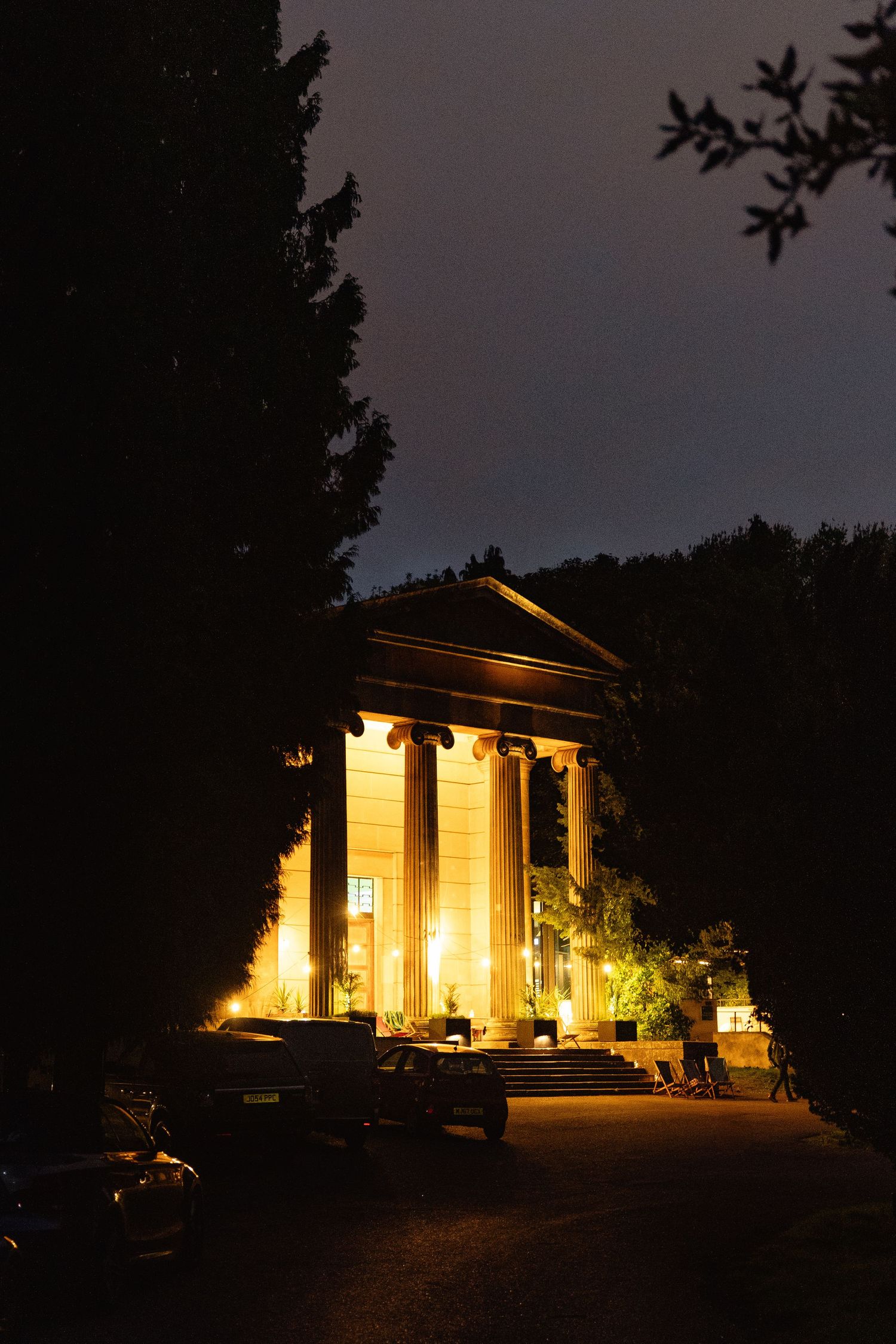 Illuminated neoclassical temple with columns glowing golden at night, surrounded by trees in a serene park setting.