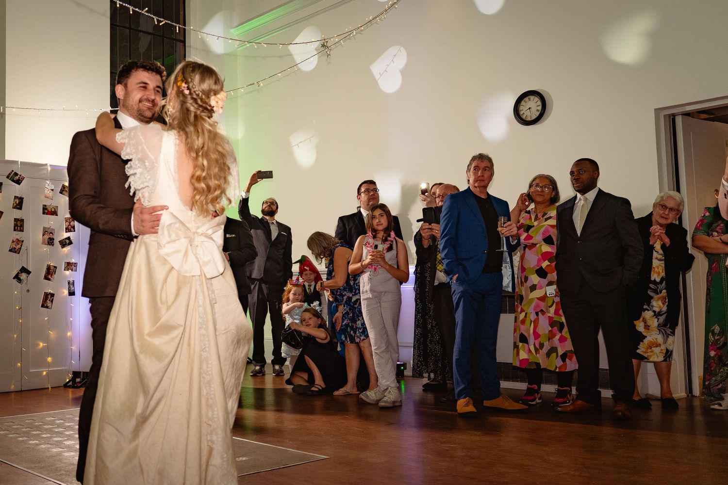Newlyweds share their first dance at a wedding reception while guests watch and celebrate in a decorated hall.
