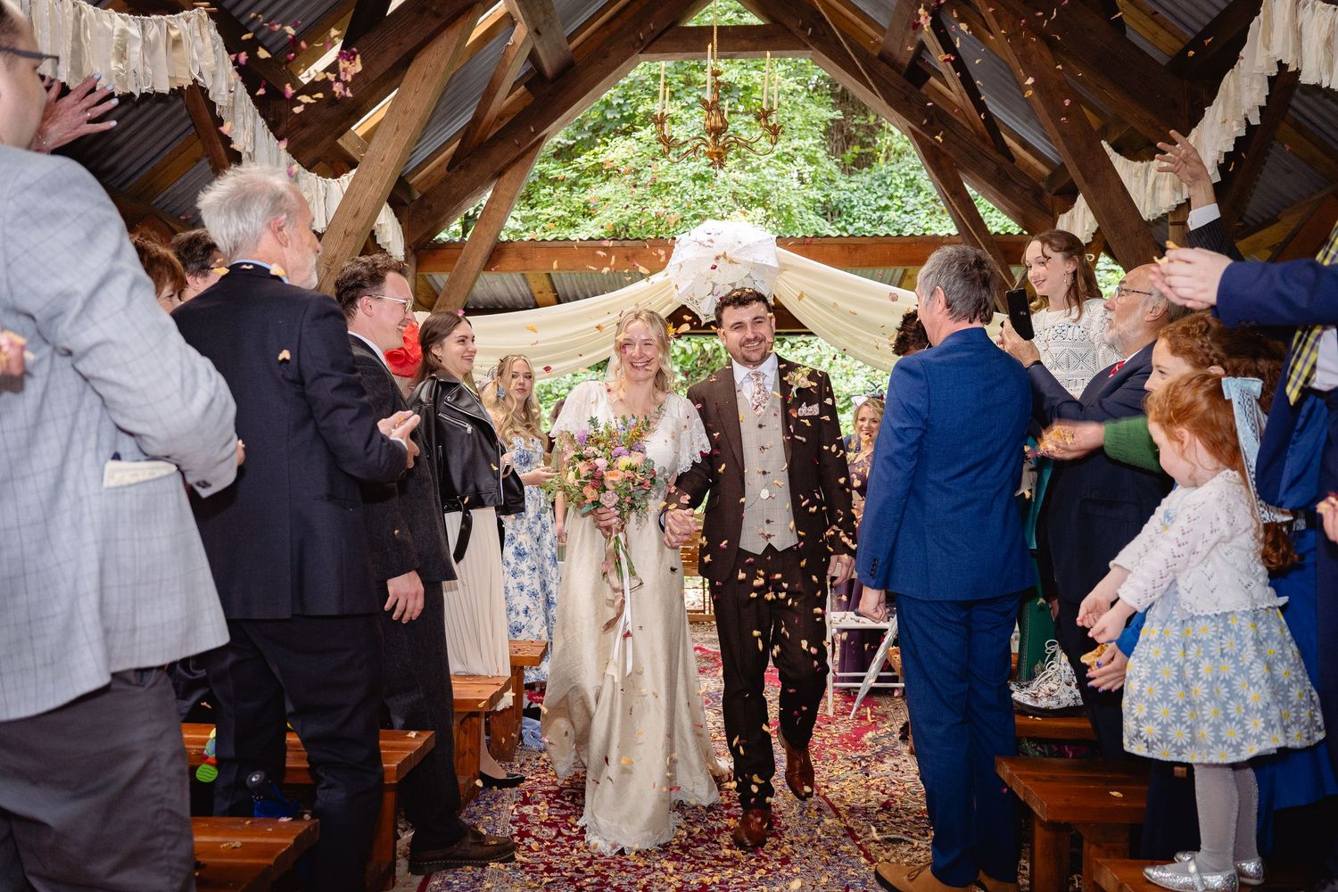 Newlyweds walk down the aisle as guests shower them with colorful confetti in a rustic chapel.